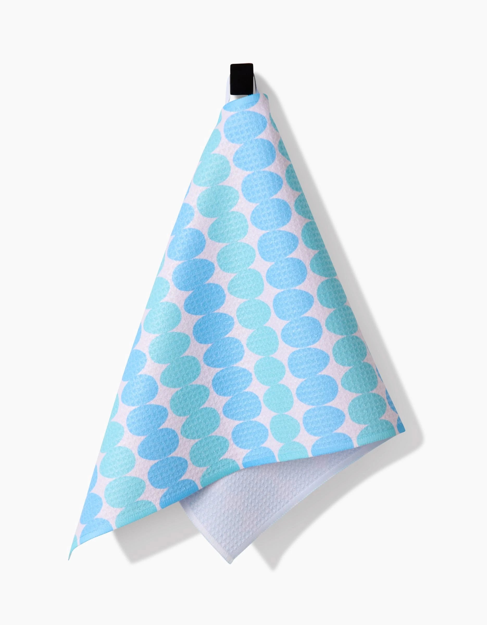 The Kayla Ann Robins Egg bar towel, made from recycled materials, features blue and teal overlapping circles and hangs from a black loop against a plain white background.