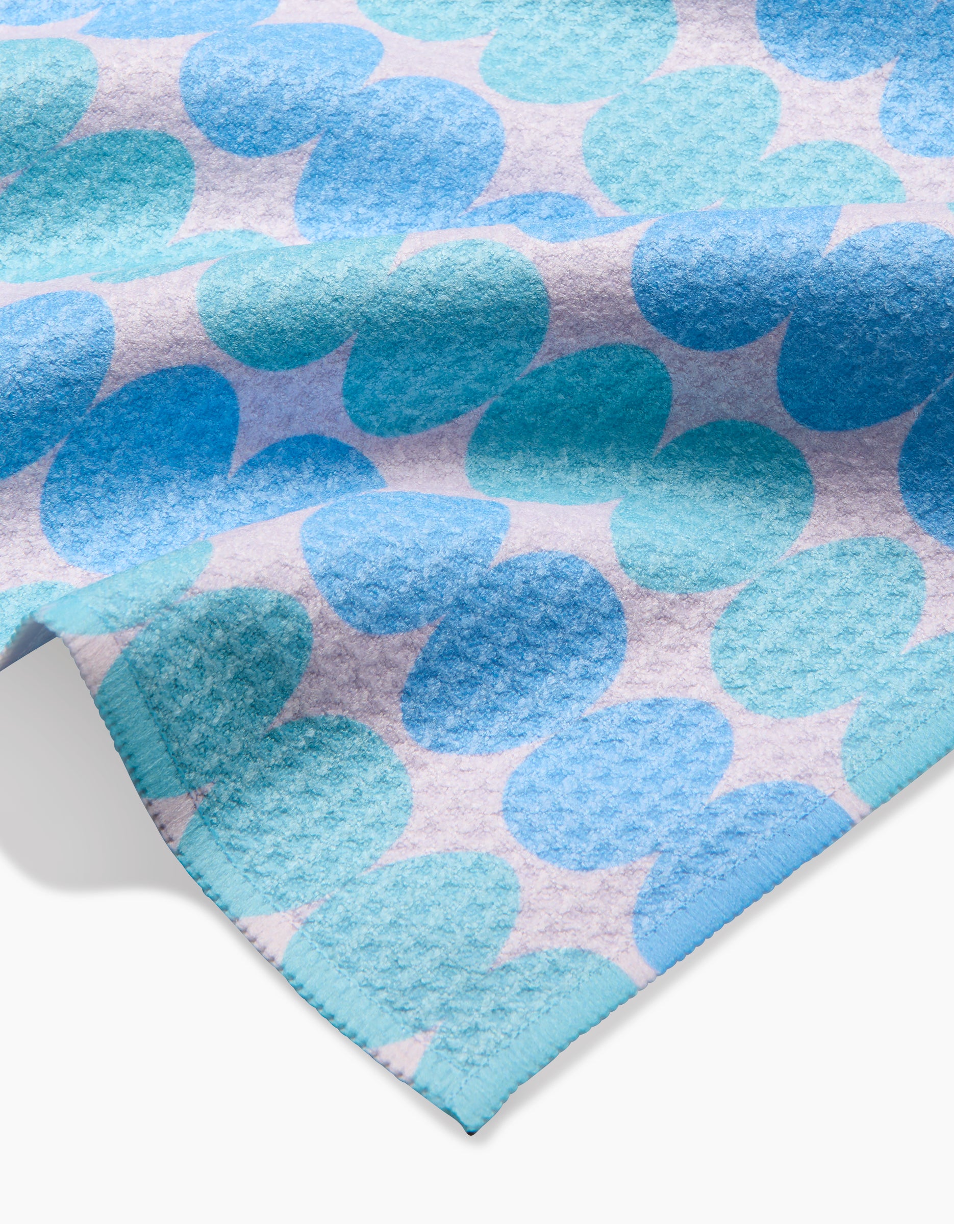 A close-up of the Kayla Ann Robins Egg Bar Towel, showcasing a pattern of overlapping blue and aqua circles on a light background with Geoweave fabric and a neatly stitched blue edge.