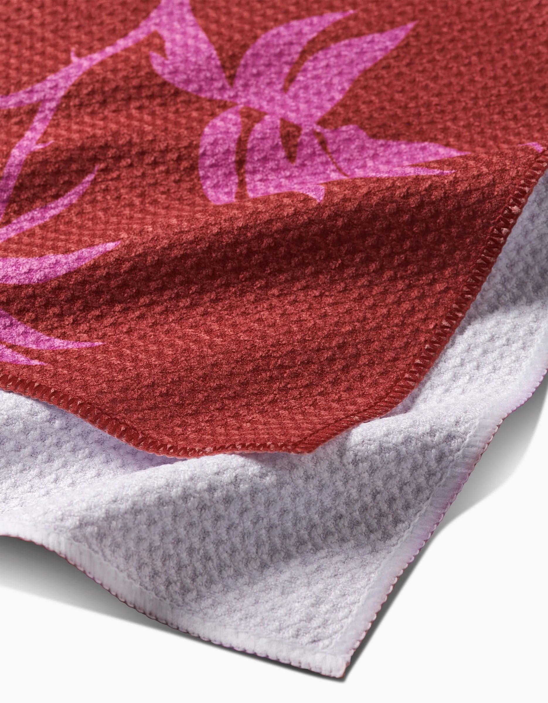 A close-up of PrintedPlant’s Rose towel, a textured red bar towel featuring a purple floral pattern and white underside, made from recycled materials.