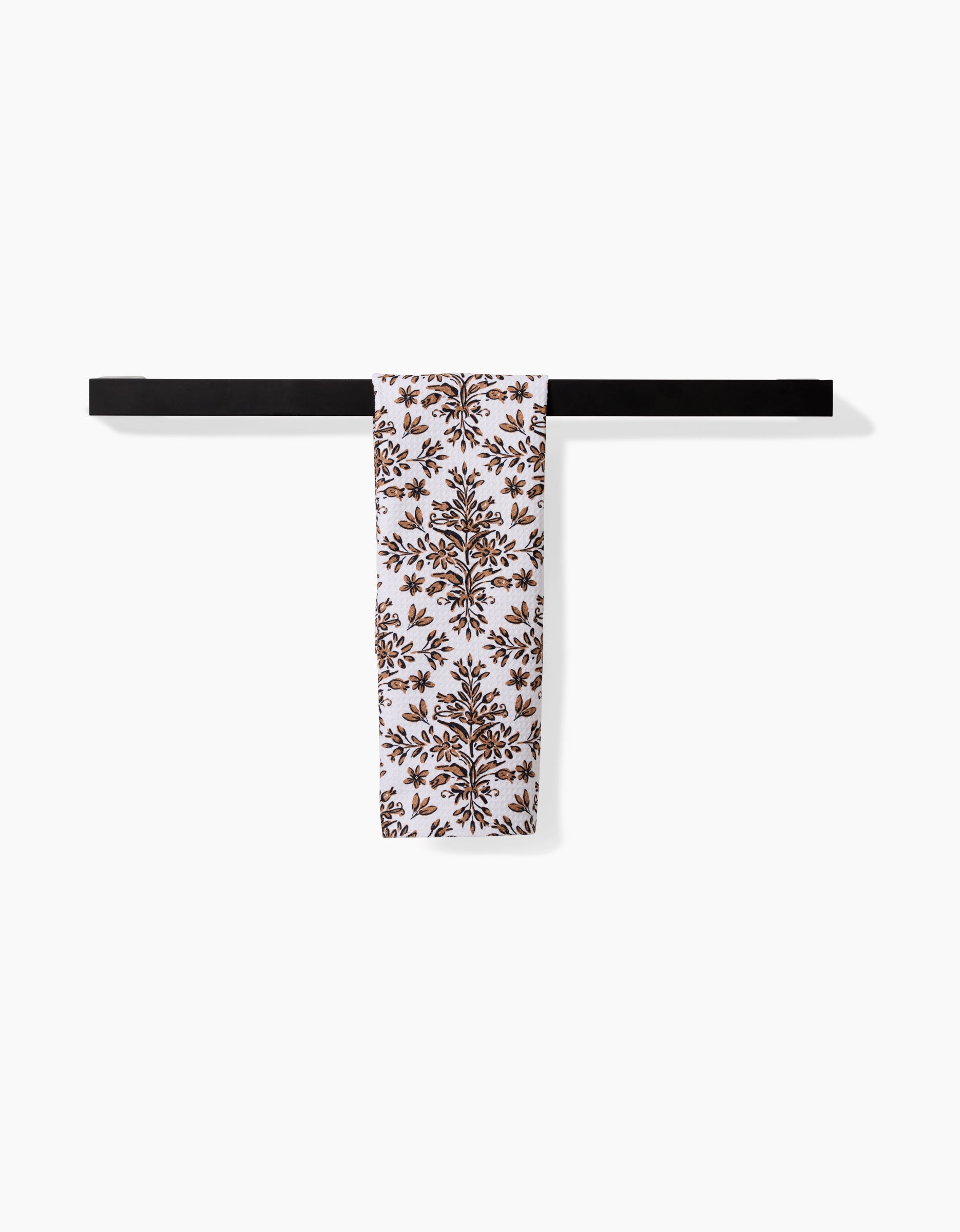 The Hufton Studio Rustic Lacy Tile Natural towel, featuring a brown floral design on white, hangs neatly over a sleek black rod against a plain white background.