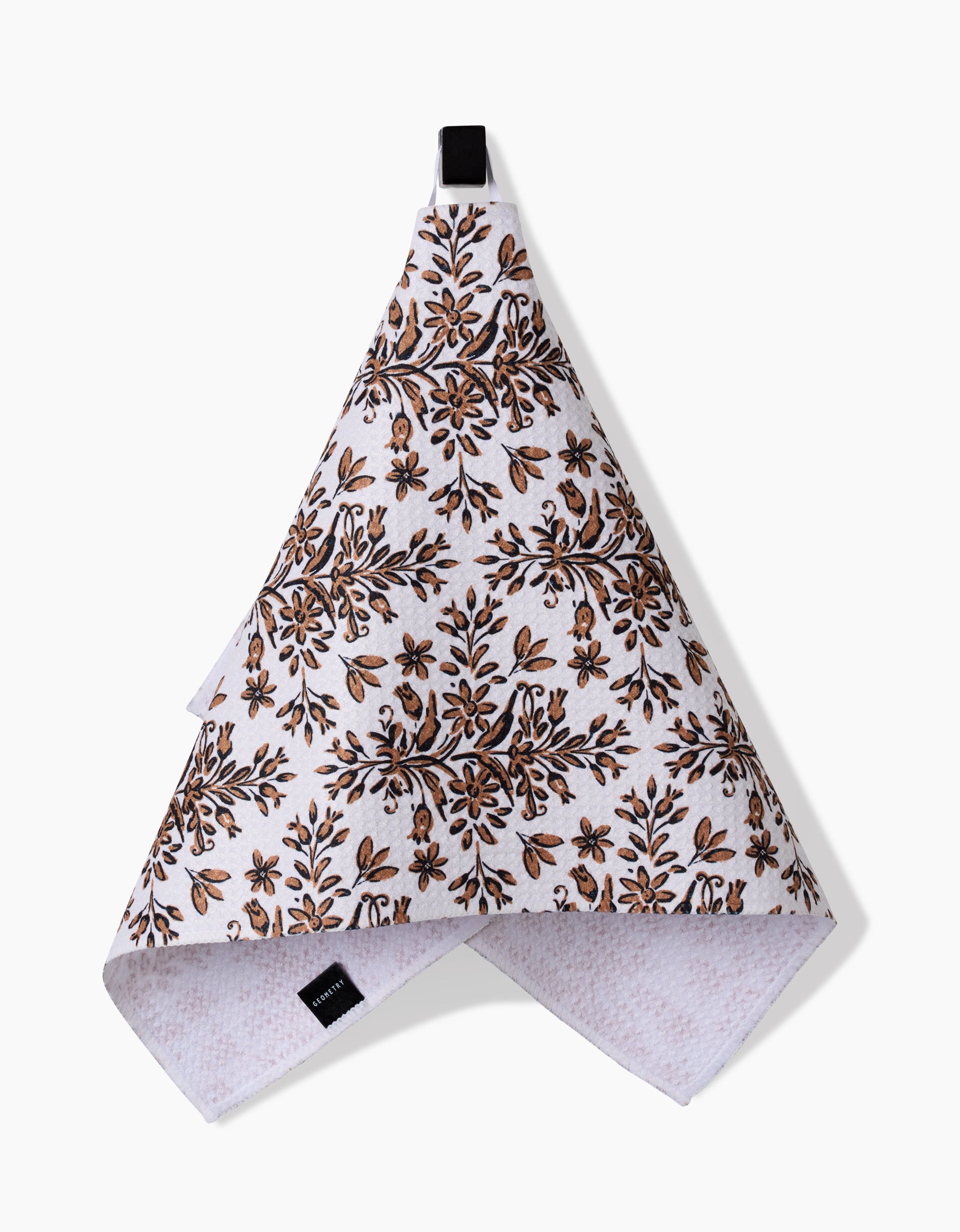 The Hufton Studio Rustic Lacy Tile Natural is a white recycled kitchen towel with a black hanging loop and a brown and black floral pattern, shown ultra-absorbent and hanging against a plain white background.