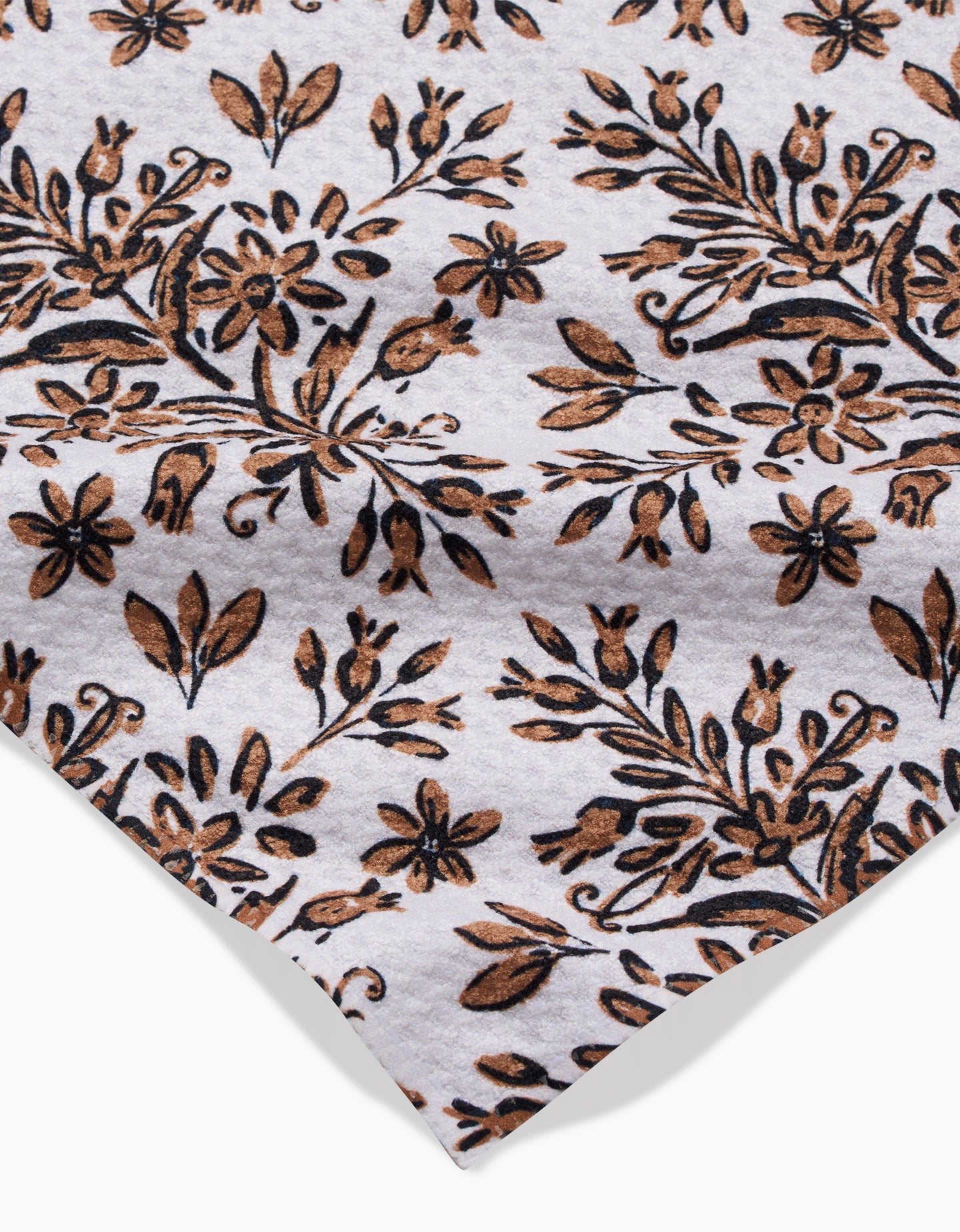 A close-up of the Rustic Lacy Tile Natural by Hufton Studio, a white ultra-absorbent towel with a brown and black floral pattern of densely arranged leaves and small flowers.