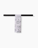 The Sage Pumpkin Field bar towel by Charlie Rowan Designs, featuring a black pumpkin pattern on white and crafted from recycled materials, is neatly folded over a simple black bar against a plain white background.
