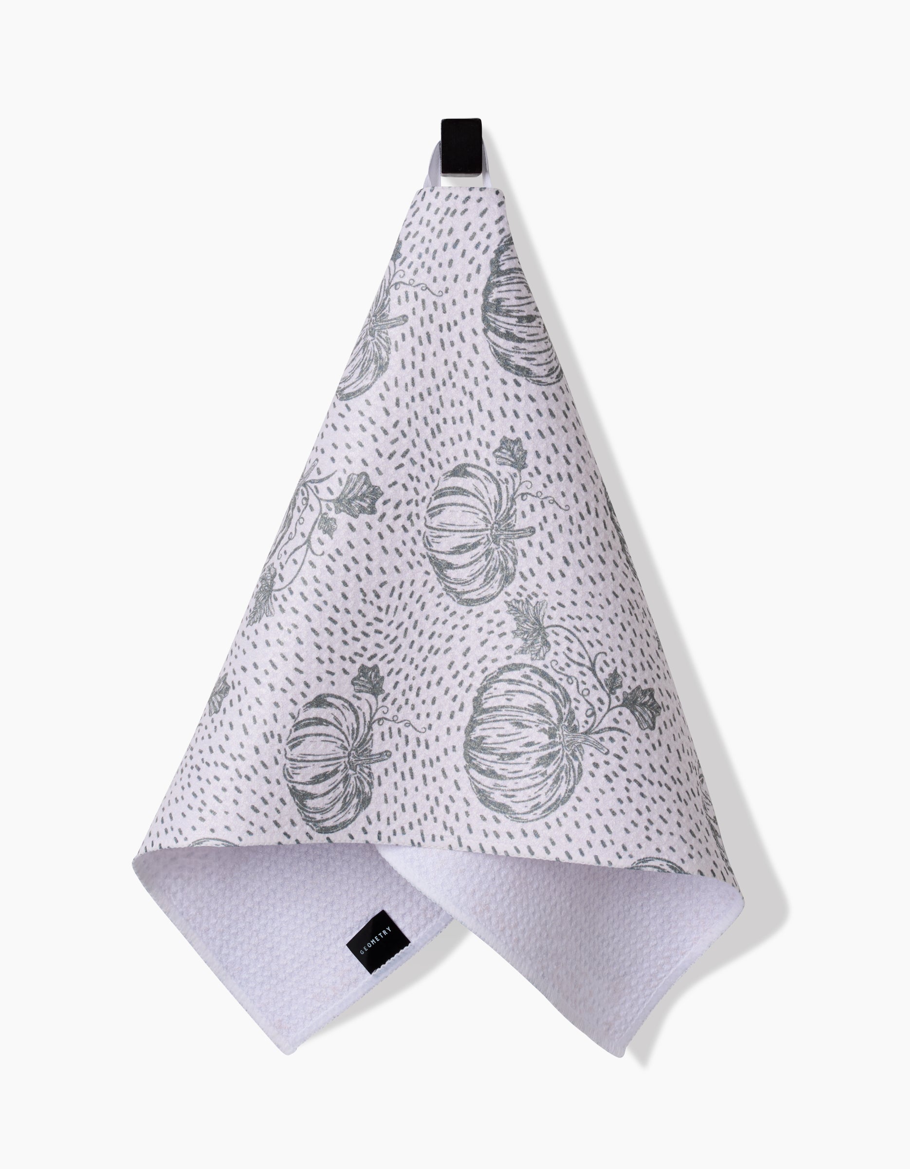 The Sage Pumpkin Field Bar Towel by Charlie Rowan Designs, crafted from Geoweave fabric, features gray pumpkin illustrations and dotted patterns. It hangs from a black loop against a white background.