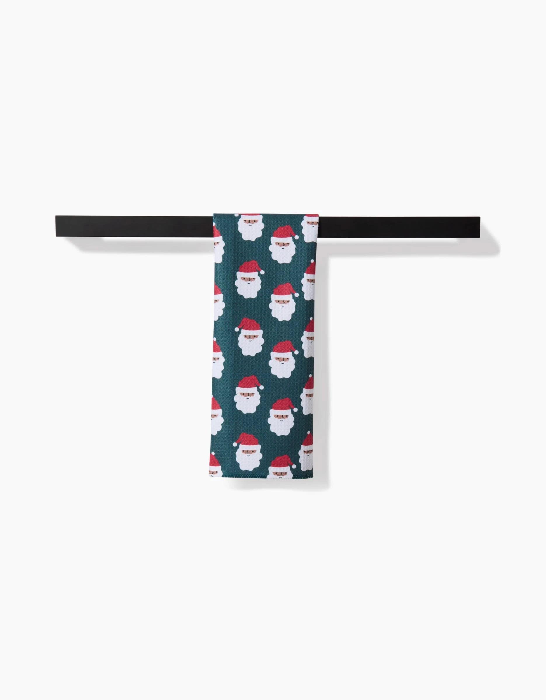 The Santa Santa towel by Charlie Rowan Designs, featuring ultra-absorbent fabric and a playful Santa Claus pattern, hangs neatly over a black towel bar against a white background.