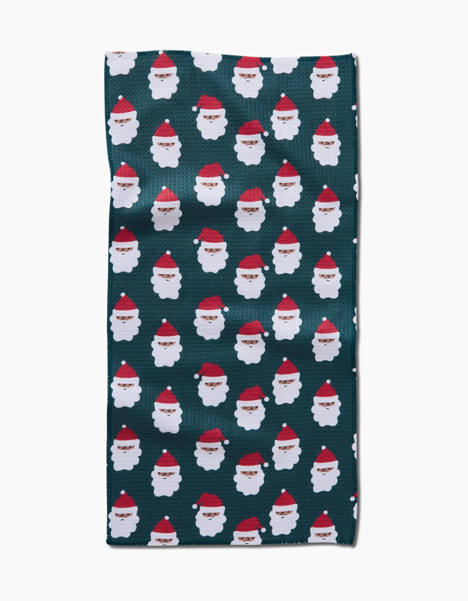 The Santa Santa bar towel by Charlie Rowan Designs is a rectangular dark green towel with a repeating pattern of small Santa faces in red hats and white beards, made from recycled materials.