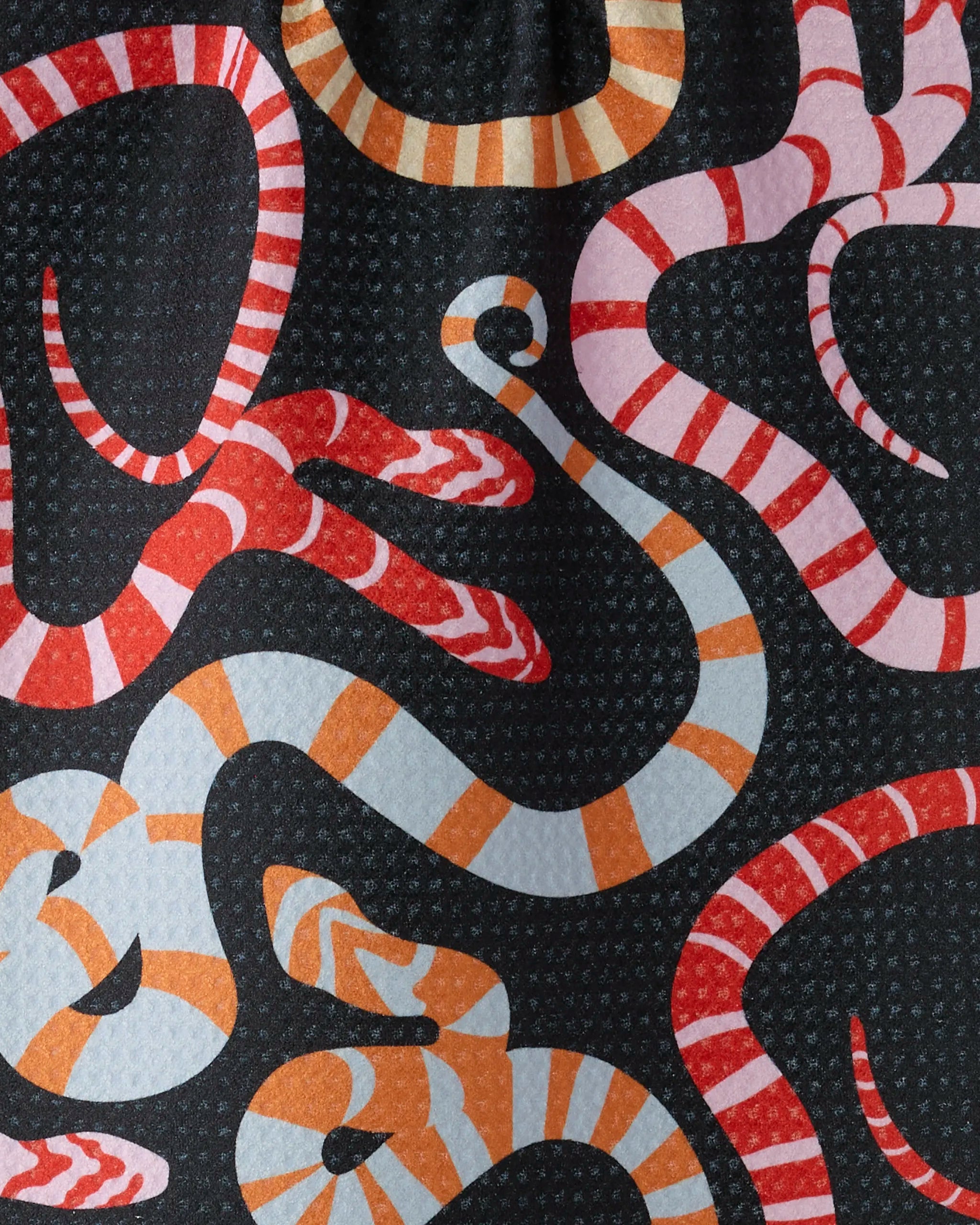Serpentine Riot by Geometry features coiled snakes with red, white, or orange stripes against a black dotted background, creating a lively, bold pattern—perfect for an ultra-absorbent towel.