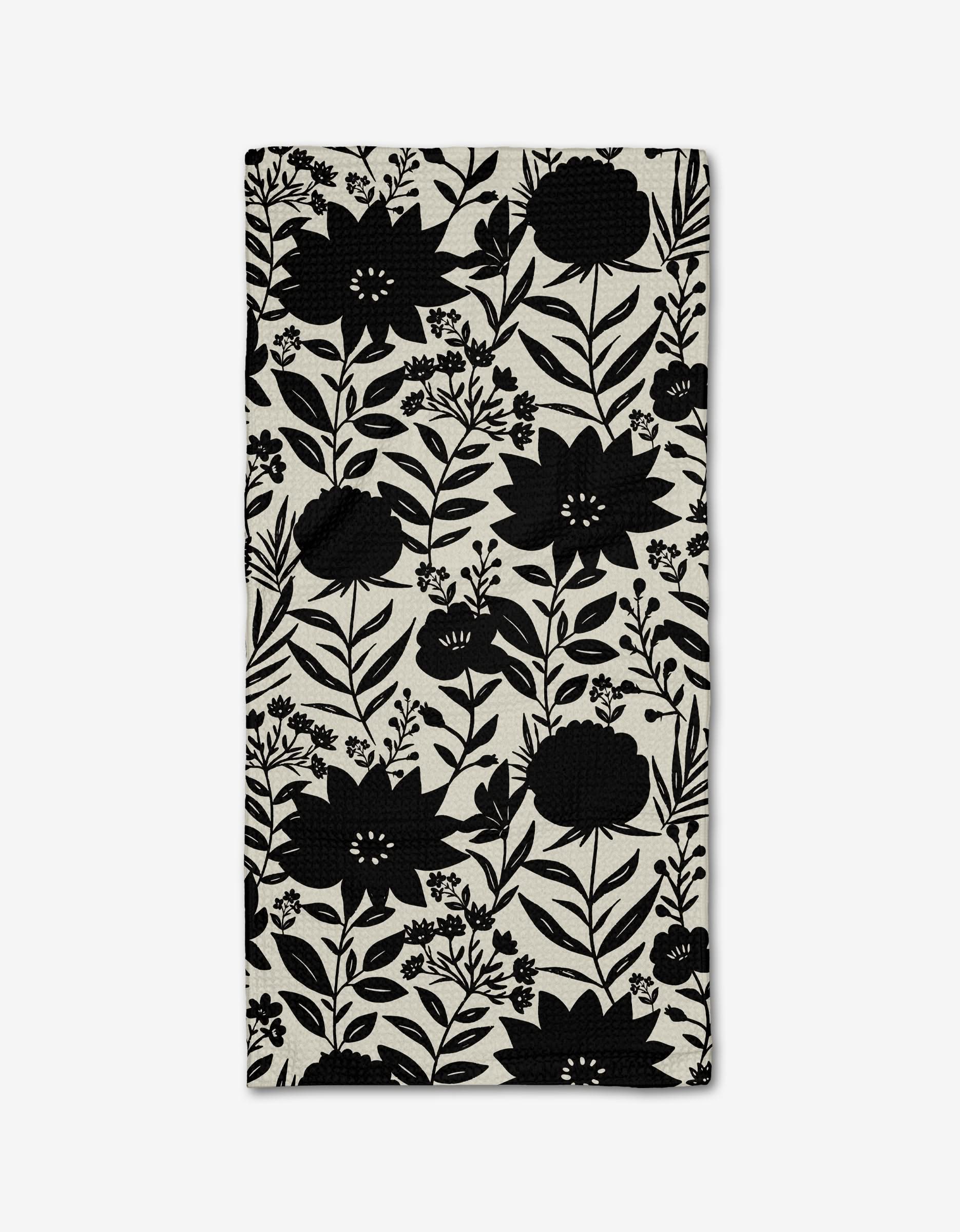 The “Shadow Flower” Bar Towel by Danelys Sidron is a rectangular beige towel made from Geoweave™ fabric, showcasing a striking black floral pattern of large flowers, leaves, and branches on a plain white background.