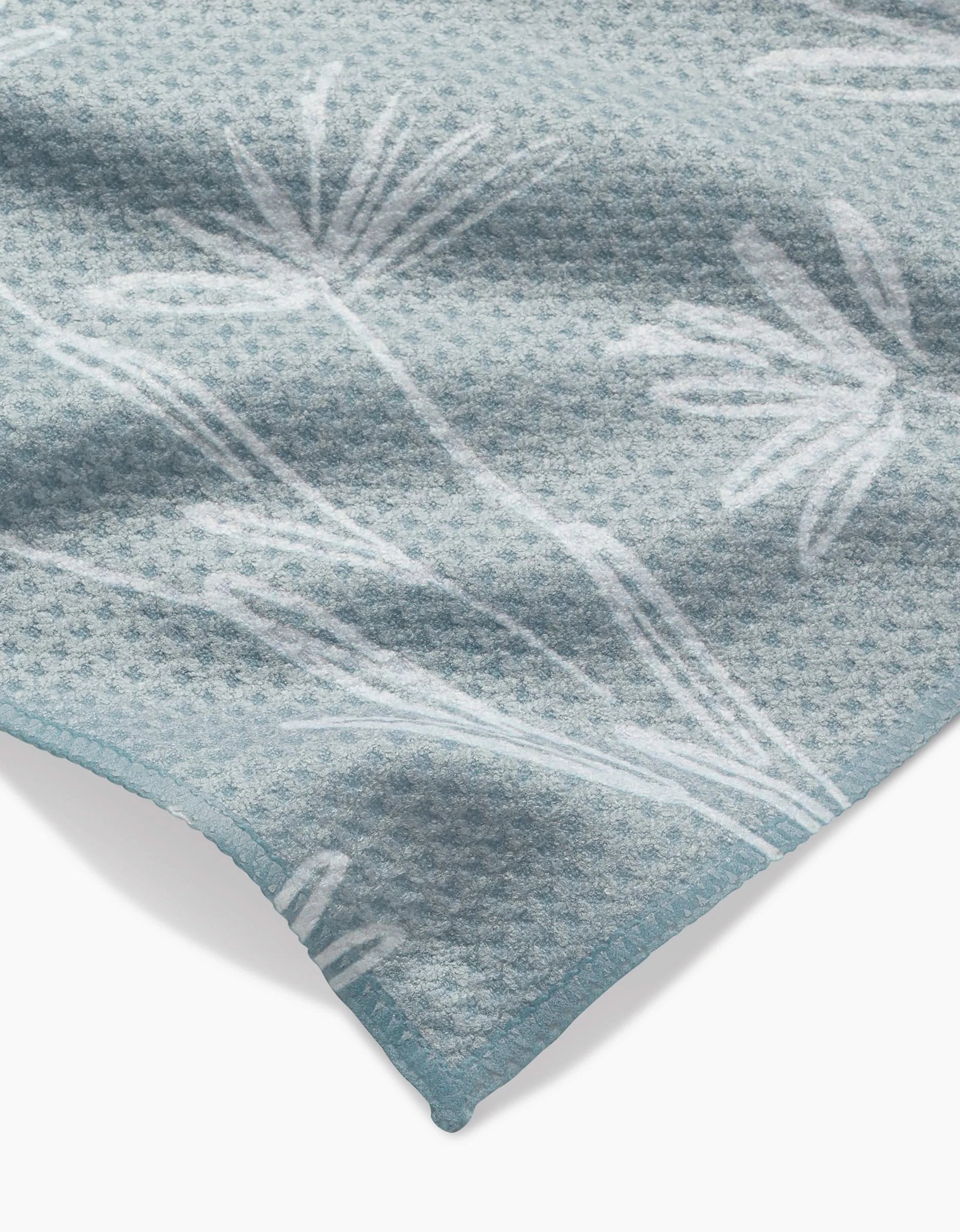 A close-up of Toboggan Avenues Sketchbook Floral Bar Towel in light blue Geoweave fabric, featuring a subtle white botanical pattern and a neatly finished corner.