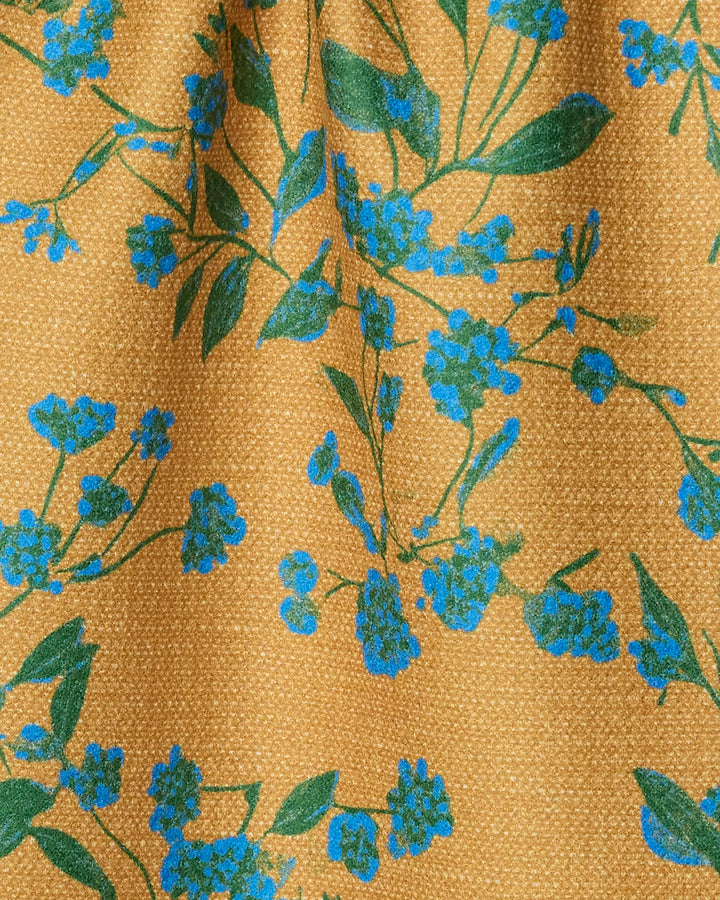Close-up of Geometry's Soleado bar towel, crafted from recycled materials. The yellow fabric features a textured surface with green leaf patterns and blue flower clusters, accented by gentle folds and soft shadows.