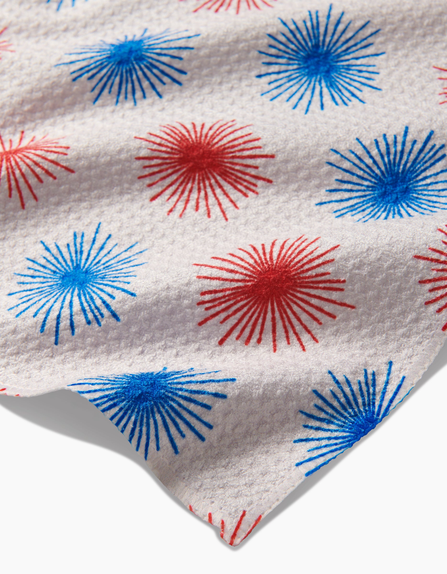 The Kayla Ann Sparkler Splash bar towel features white Geoweave fabric with a repeating red and blue starburst fireworks pattern printed across its textured surface.