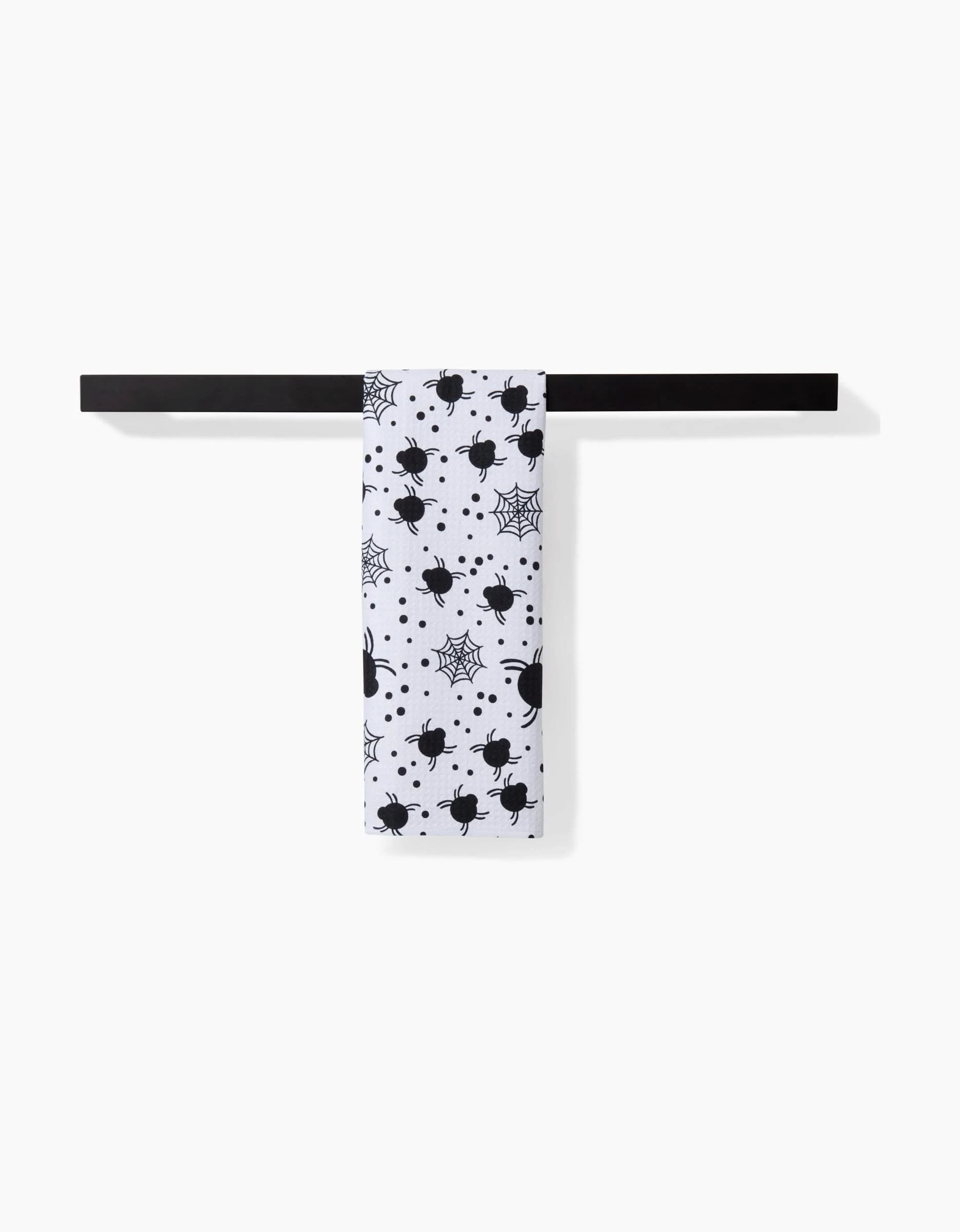 The Spiders For Days towel by Charlie Rowan Designs, featuring black spider and web patterns, is draped over a sleek black bar against a plain white backdrop.