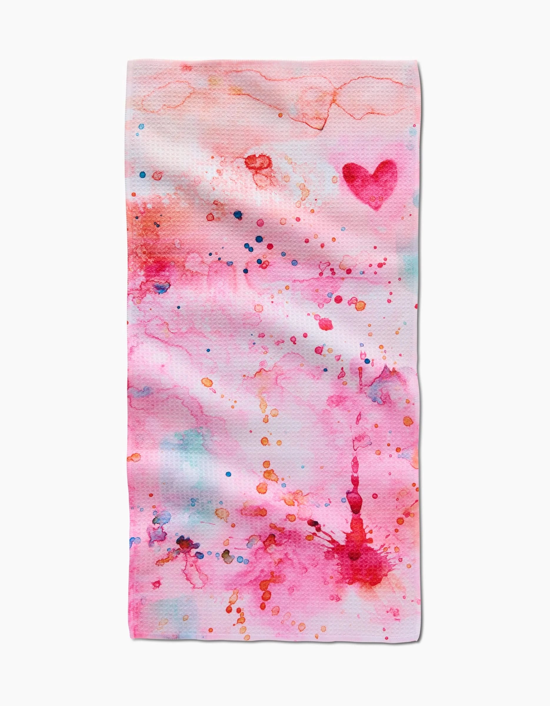The Sara Mari Splash of Love towel is ultra-absorbent and white, featuring abstract pink, red, and orange watercolor splashes, small paint dots, and a solid pink heart in the upper right corner.