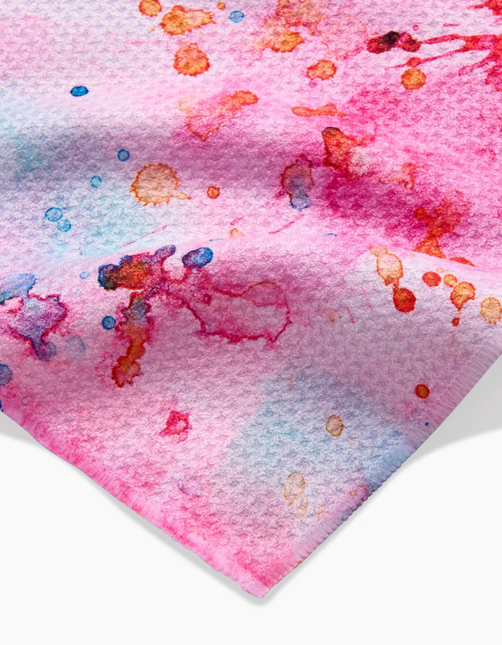 The “Splash of Love” towel by Sara Mari features a textured, ultra-absorbent fabric with abstract watercolor splatters in pink, red, blue, and orange for a vibrant, artistic look.