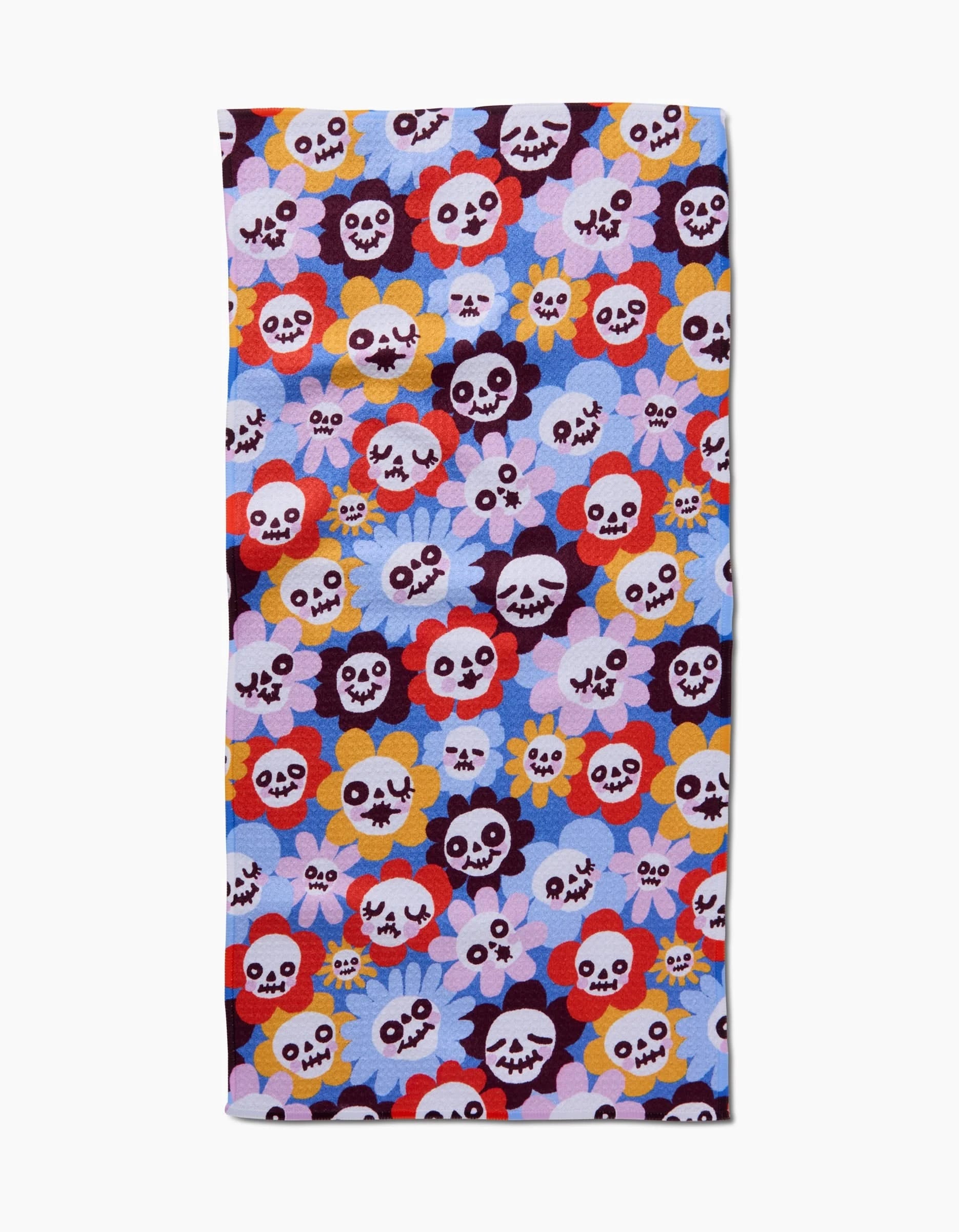 The So Lazo Spooky Bouquet bar towel features a vibrant, repeating pattern of cartoon skulls and flowers in red, yellow, purple, blue, and white on light purple. Made from ultra-absorbent recycled materials.
