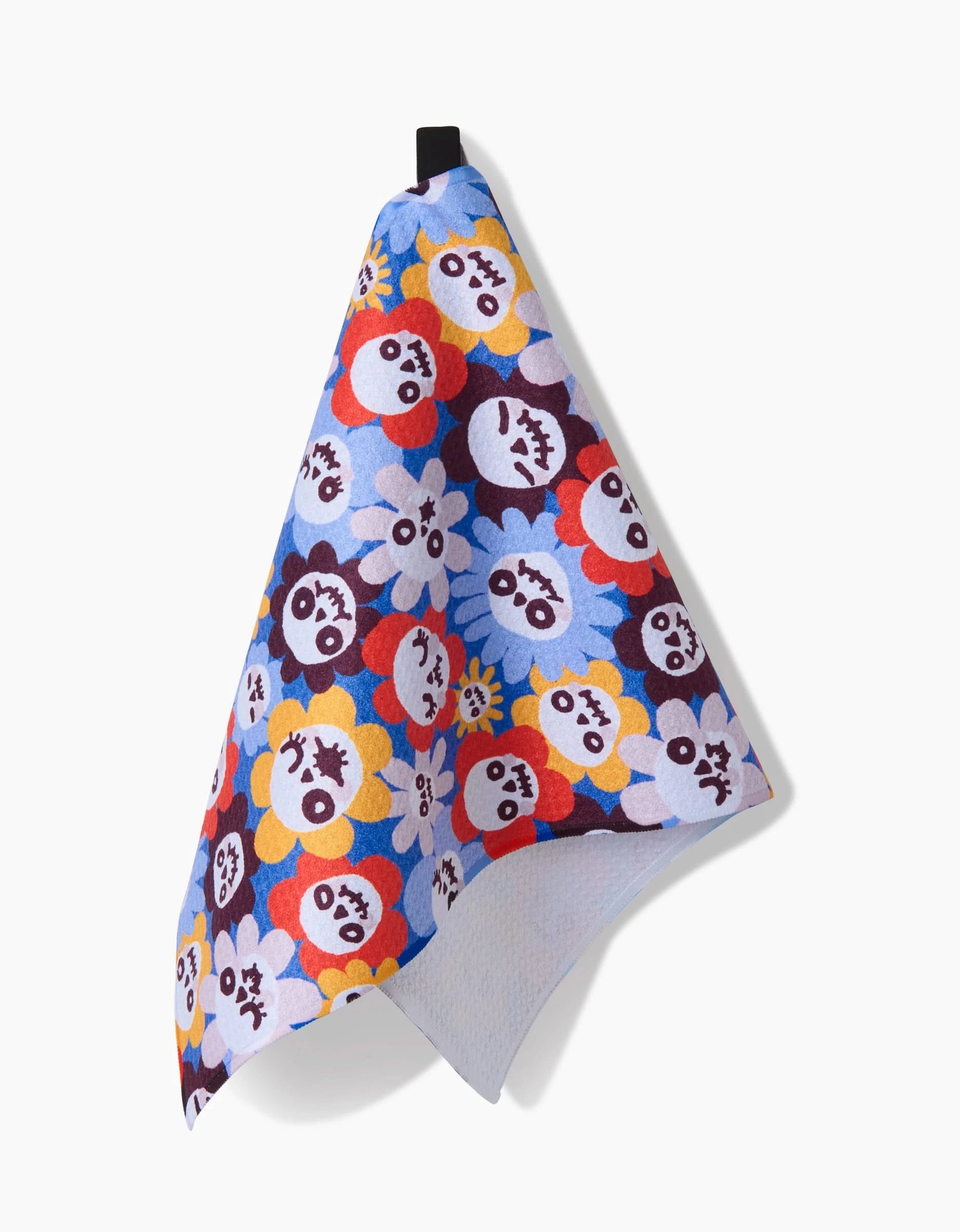 The So Lazo Spooky Bouquet towel is ultra-absorbent and features a repeating pattern of cartoon flowers in red, blue, yellow, and purple—each with a unique expression—and includes a small black loop for easy hanging.