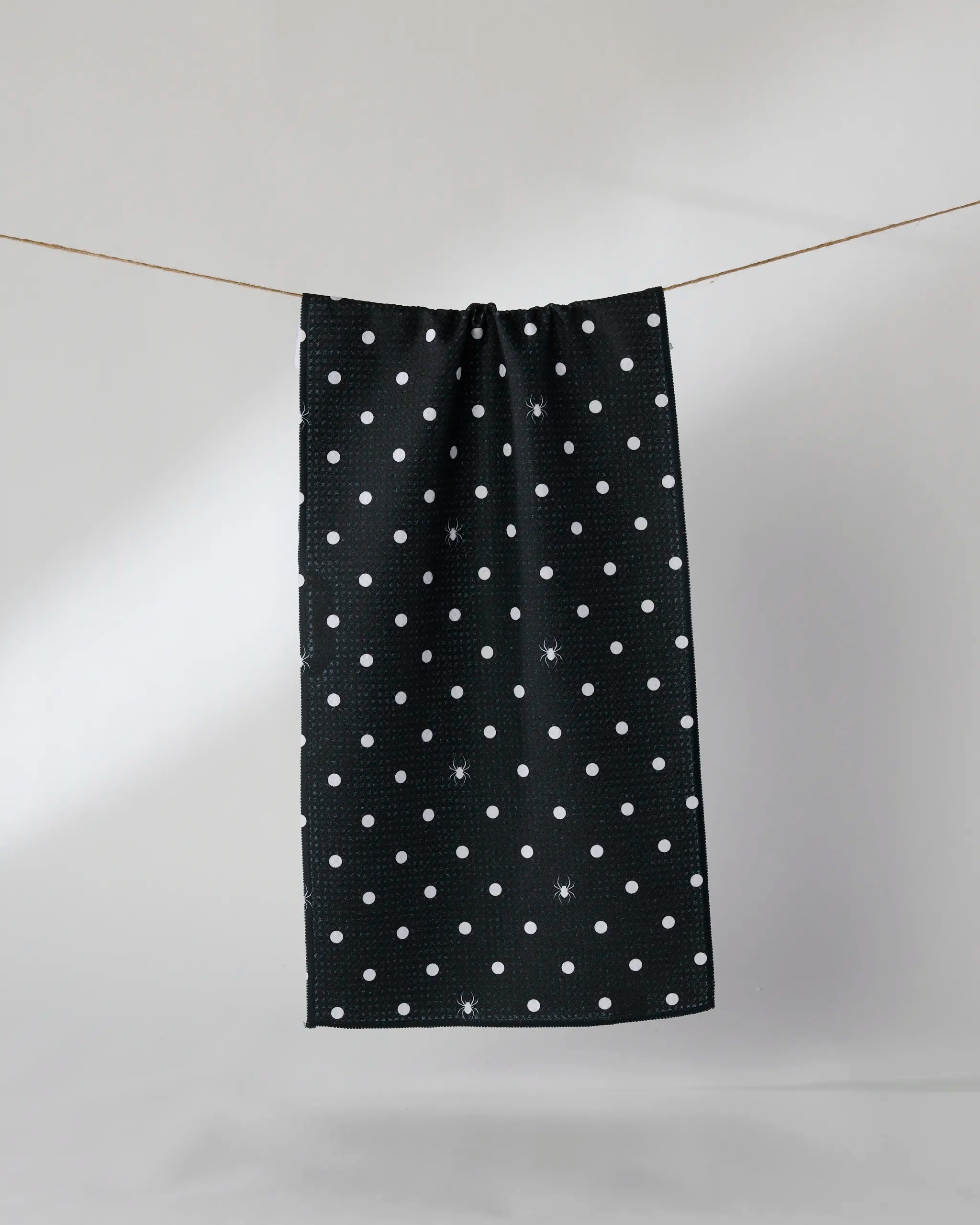The Geometry Spookydots towel, featuring ultra-absorbent fabric and a black design with evenly spaced white polka dots, hangs on a clothesline against a plain, light background.