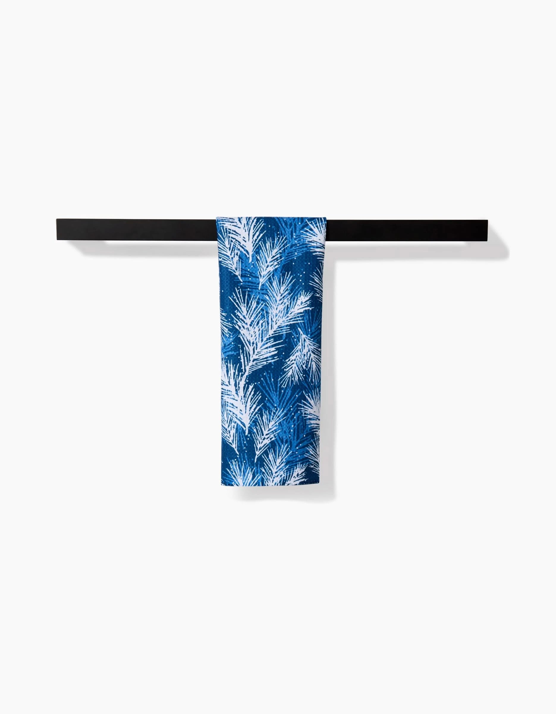 The Sprinkled Spruce bar towel by Kris Ruff features a blue design with white palm leaves, draped over a sleek black towel bar. This ultra-absorbent towel brings both style and function to your space.