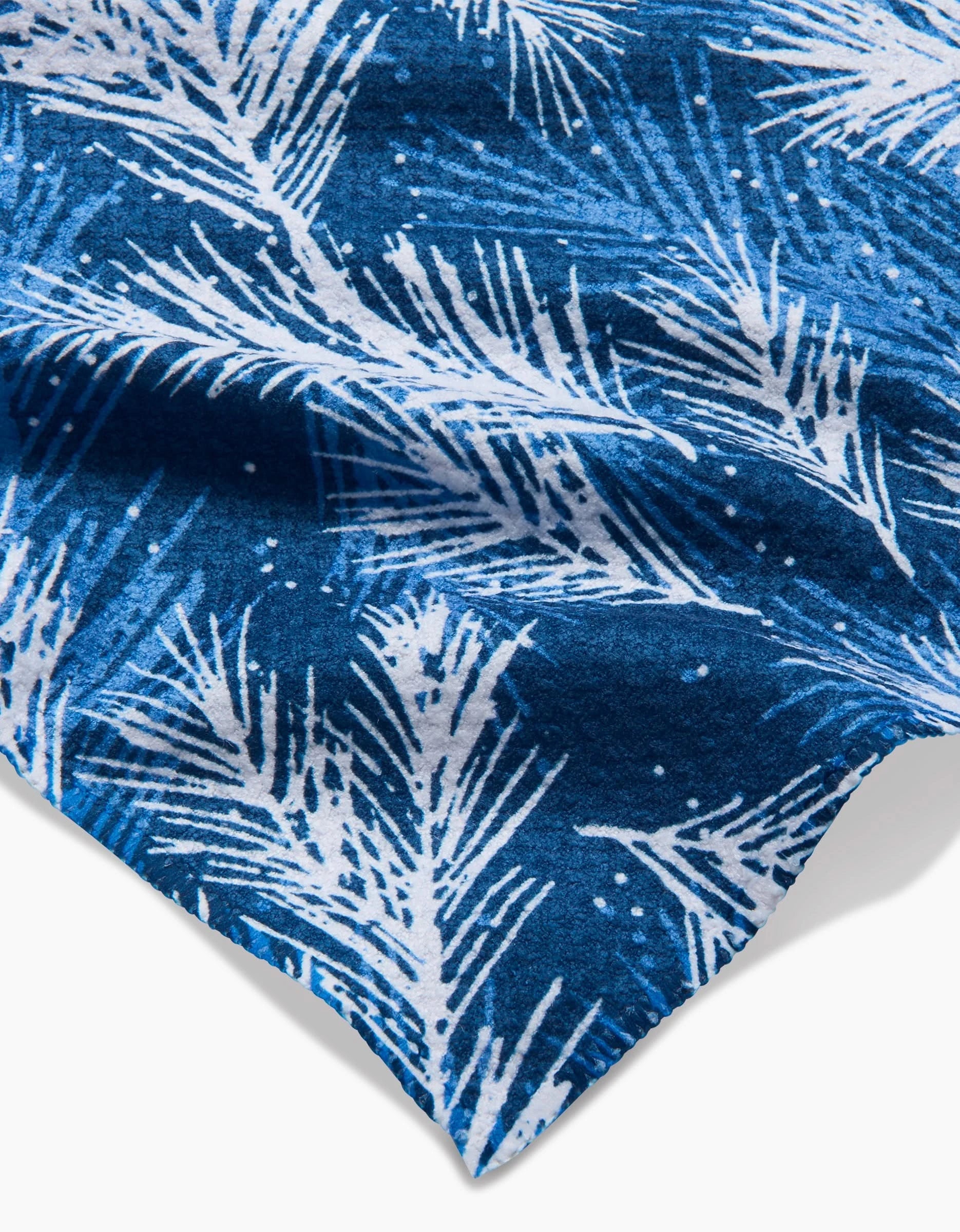 A close-up of Kris Ruff’s Sprinkled Spruce towel, featuring a blue ultra-absorbent fabric with a white palm leaf pattern and small white dots for a tropical look.