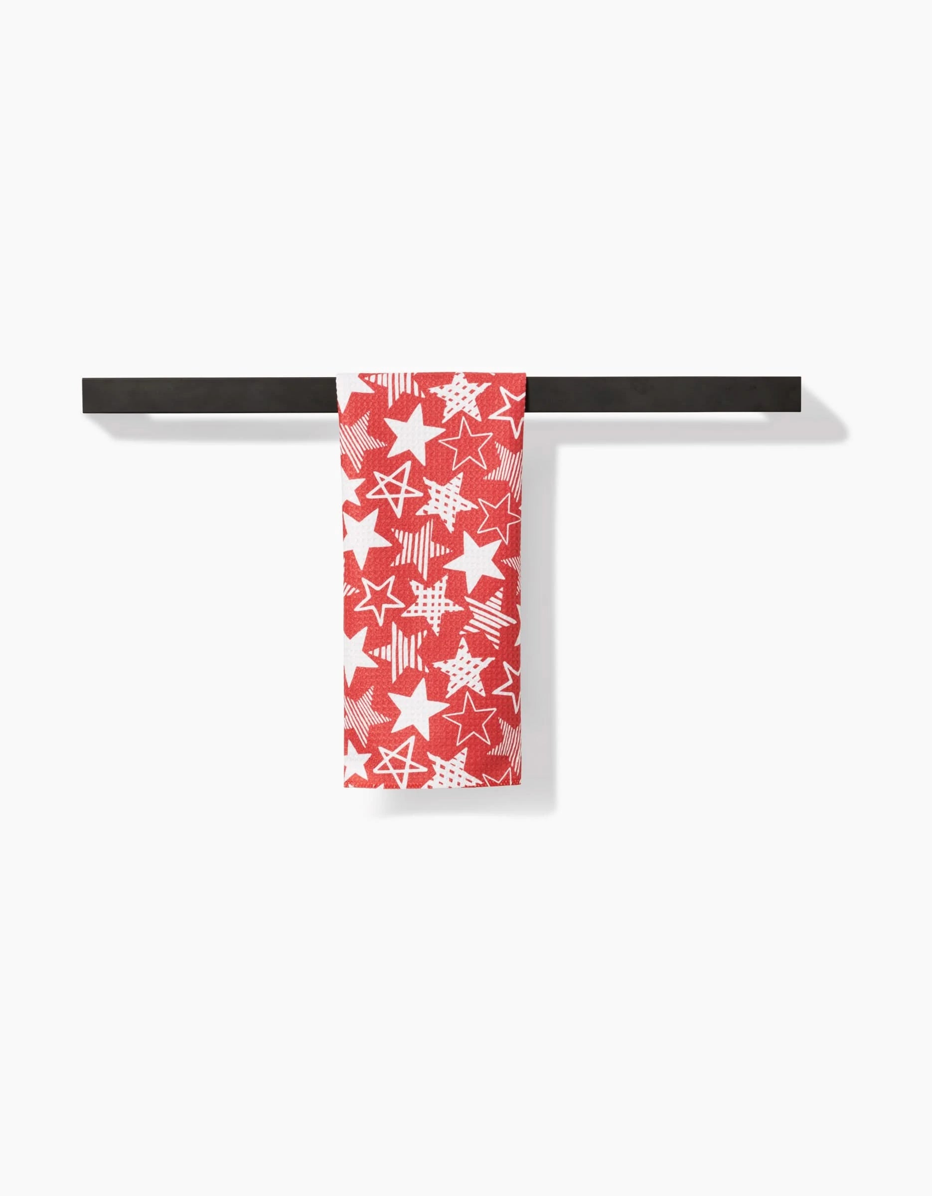 The Hufton Studio Stars In Your Eyes Red towel, made from recycled materials and adorned with star patterns in red and white, hangs neatly over a black horizontal bar against a white background.