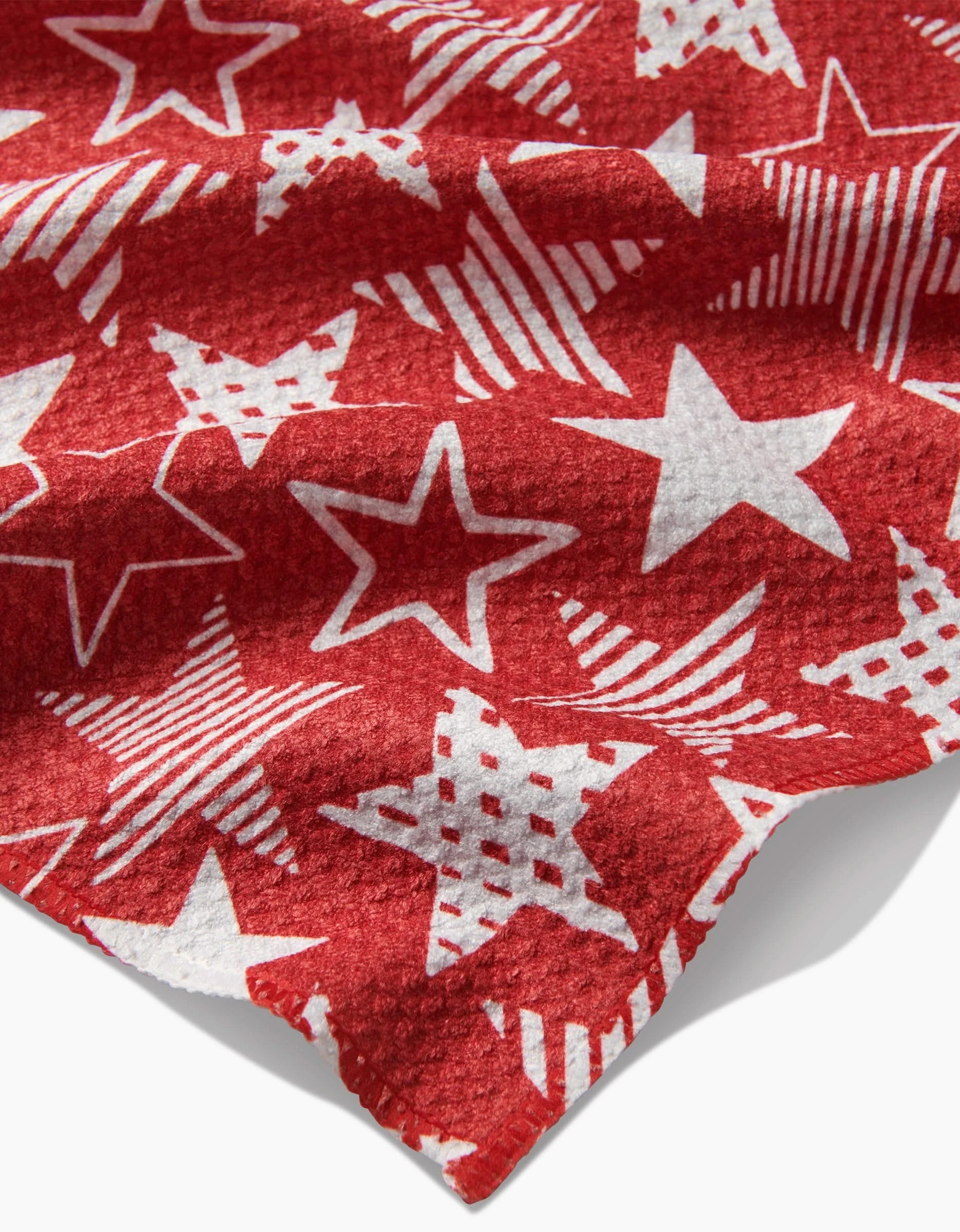 The Stars In Your Eyes Red bar towel by Hufton Studio features white stars in various designs on red Geoweave fabric. The slightly wrinkled towel shows a visible corner in the foreground.