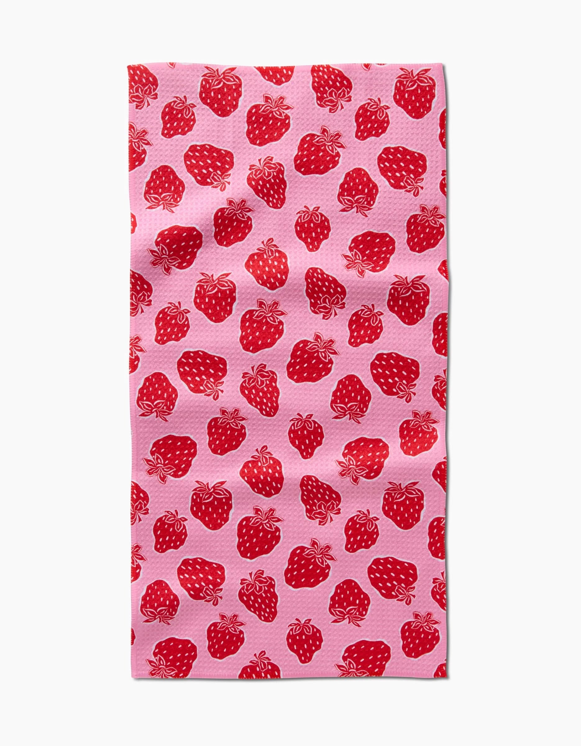 The Strawberry Fields Bar Towel by Charlie Rowan Designs, made from Geoweave fabric, features a pink background with a repeating red strawberry and green stem pattern, shown here against a white backdrop.
