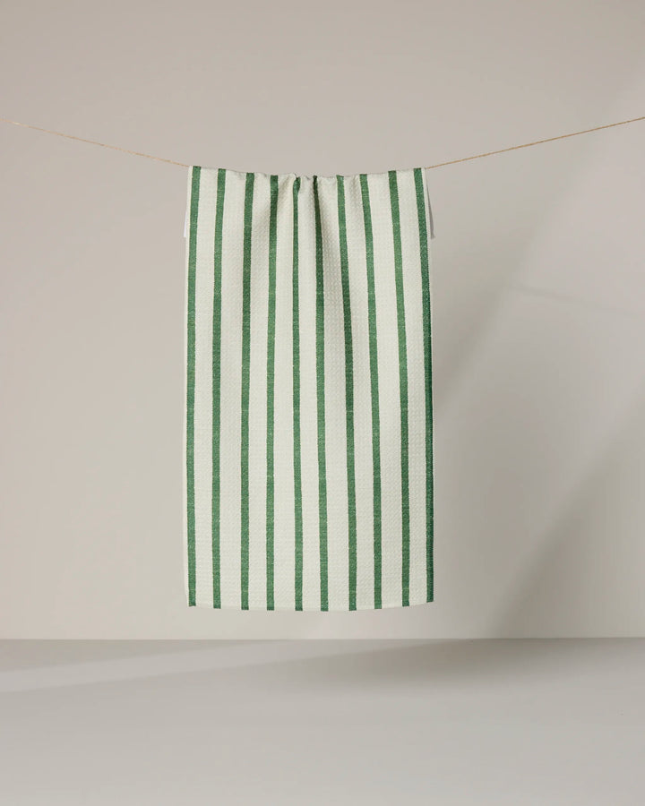The Geometry Striped Path towel, featuring ultra-absorbent fabric and vertical green stripes on white, hangs neatly on a clothesline against a light background.