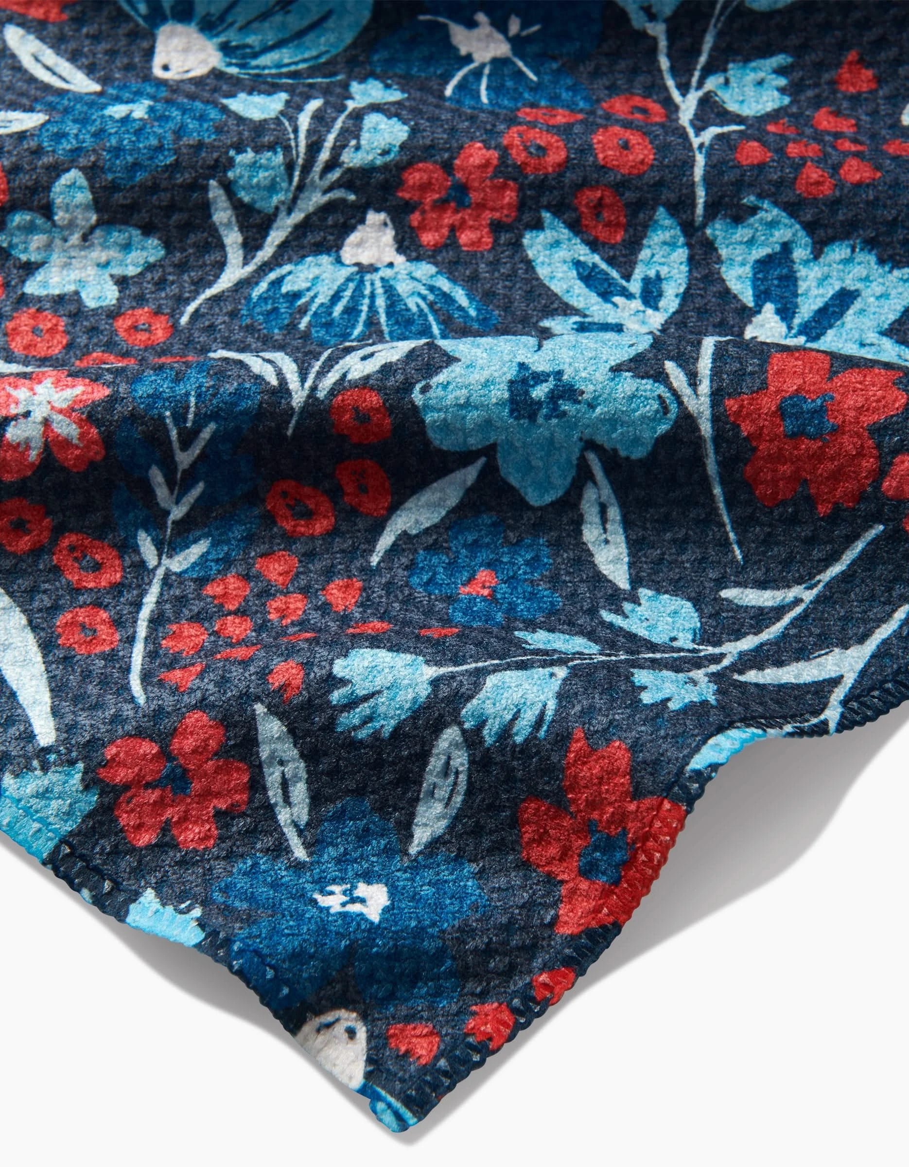 A close-up of the Summer Bloom bar towel by Hufton Studio, highlighting its vibrant red, blue, and white floral pattern on a dark base and showcasing the clear texture of the Geoweave fabric.