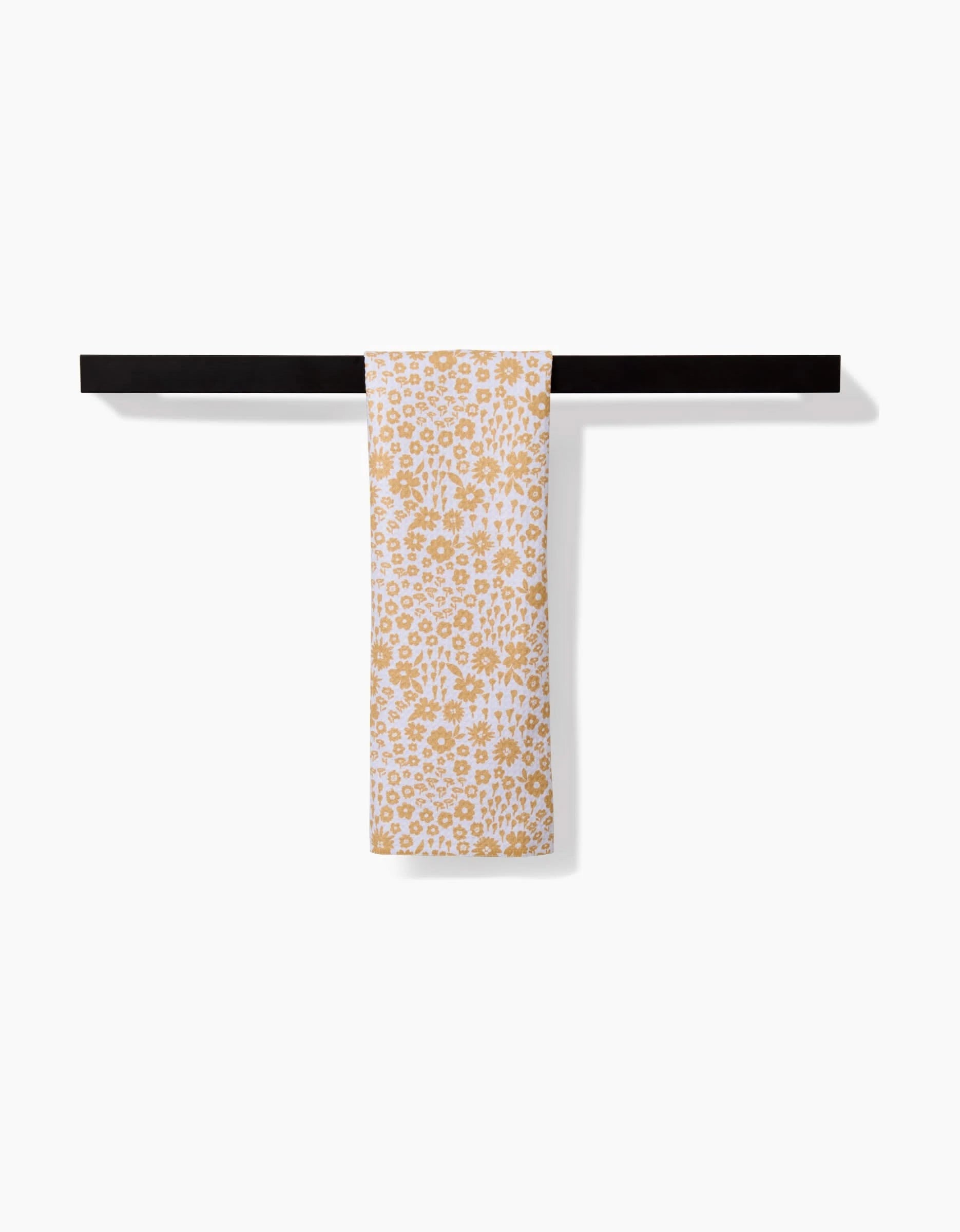 The Summer Fields bar towel by Hufton Studio, featuring a yellow floral print on white and made from recycled materials, hangs elegantly over a sleek black towel bar against a clean white background.