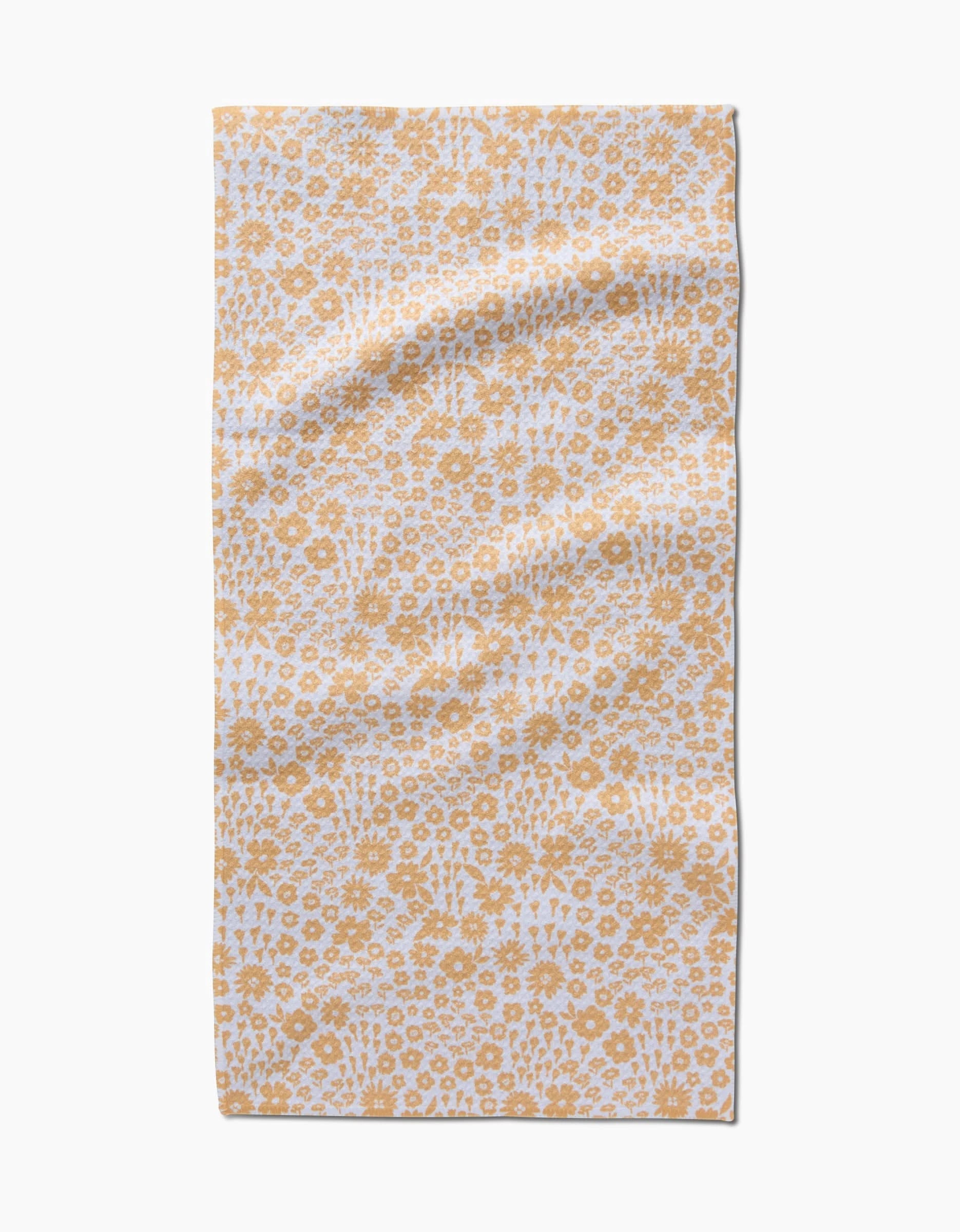 The Summer Fields bar towel by Hufton Studio features a white background with a repeating yellow floral pattern. Made from ultra-absorbent recycled materials, it’s shown laid flat with gentle creases.