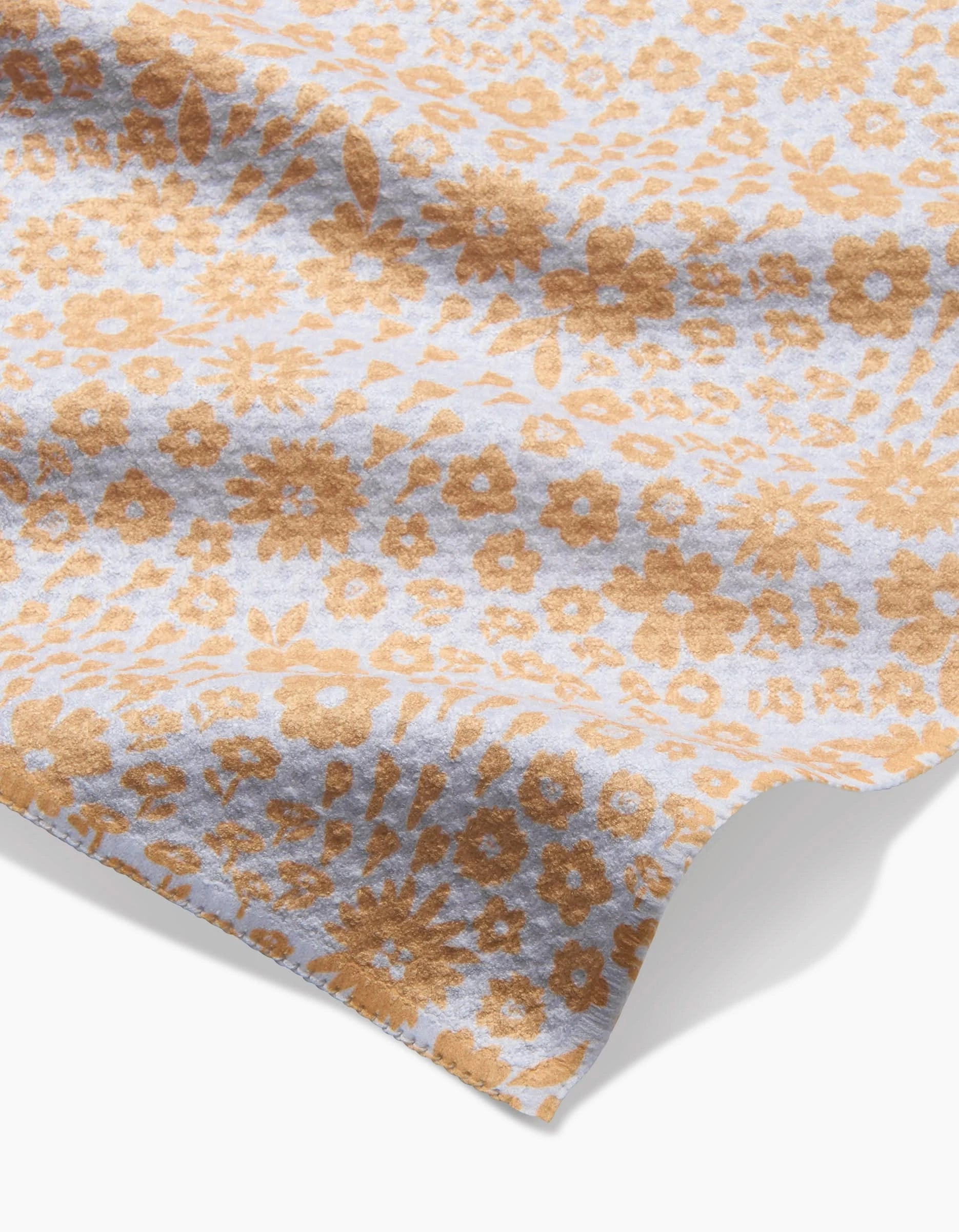 A close-up of the Hufton Studio Summer Fields bar towel, made from ultra-absorbent fabric with a light blue background and an all-over pattern of small brown flowers and leaves. The towel appears slightly wrinkled on a white surface.