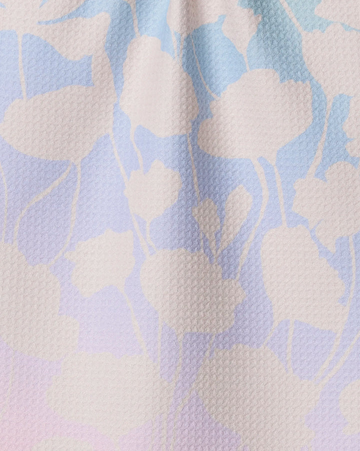 The Sunlit Silhouette kitchen towel by Geometry features a textured, eco-friendly fabric with white leaf and stem silhouettes over a pastel gradient of blue, pink, and lavender.
