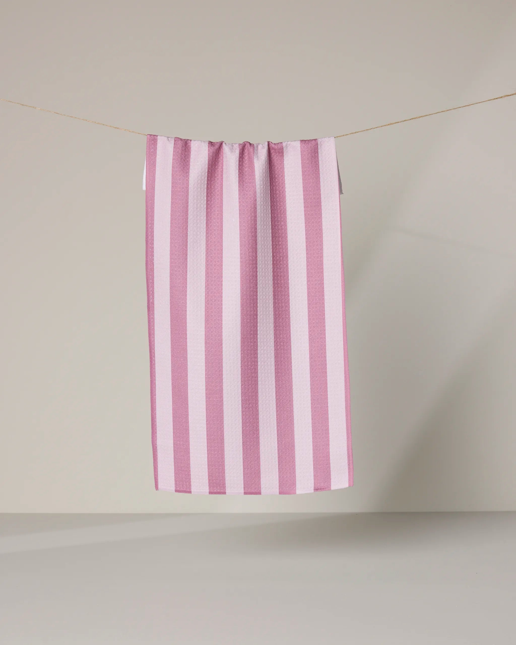 The Geometry Swan Stripe kitchen towel, featuring pink and white stripes, hangs on a clothesline against a plain light background.