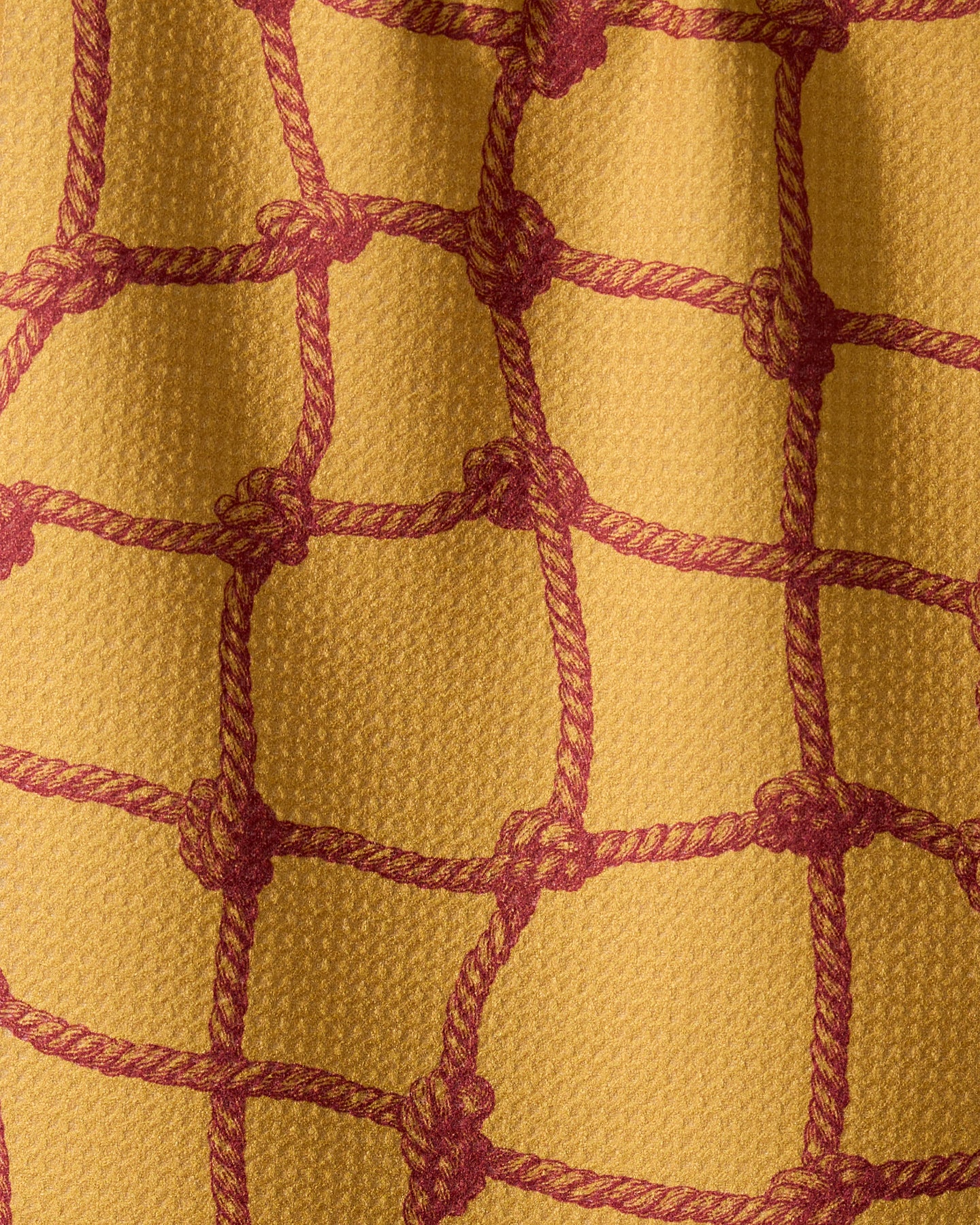Tethered Orange by Geometry features yellow textured fabric with red rope-like lines forming rectangle patterns, resembling a net. The quick-drying towel has visible folds and shadows that enhance its depth and design.