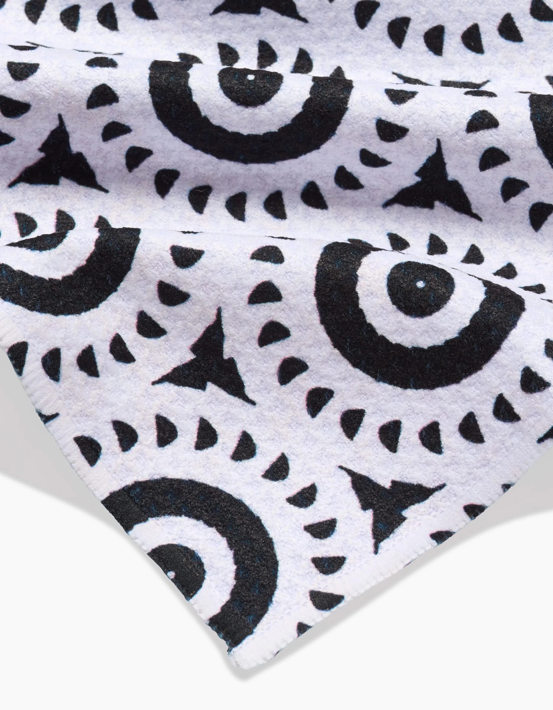 A close-up of the Katherine Berkeley Texas Two Step bar towel shows white Geoweave fabric with black circular and triangular abstract patterns in rows. The towel is slightly folded at the corner.