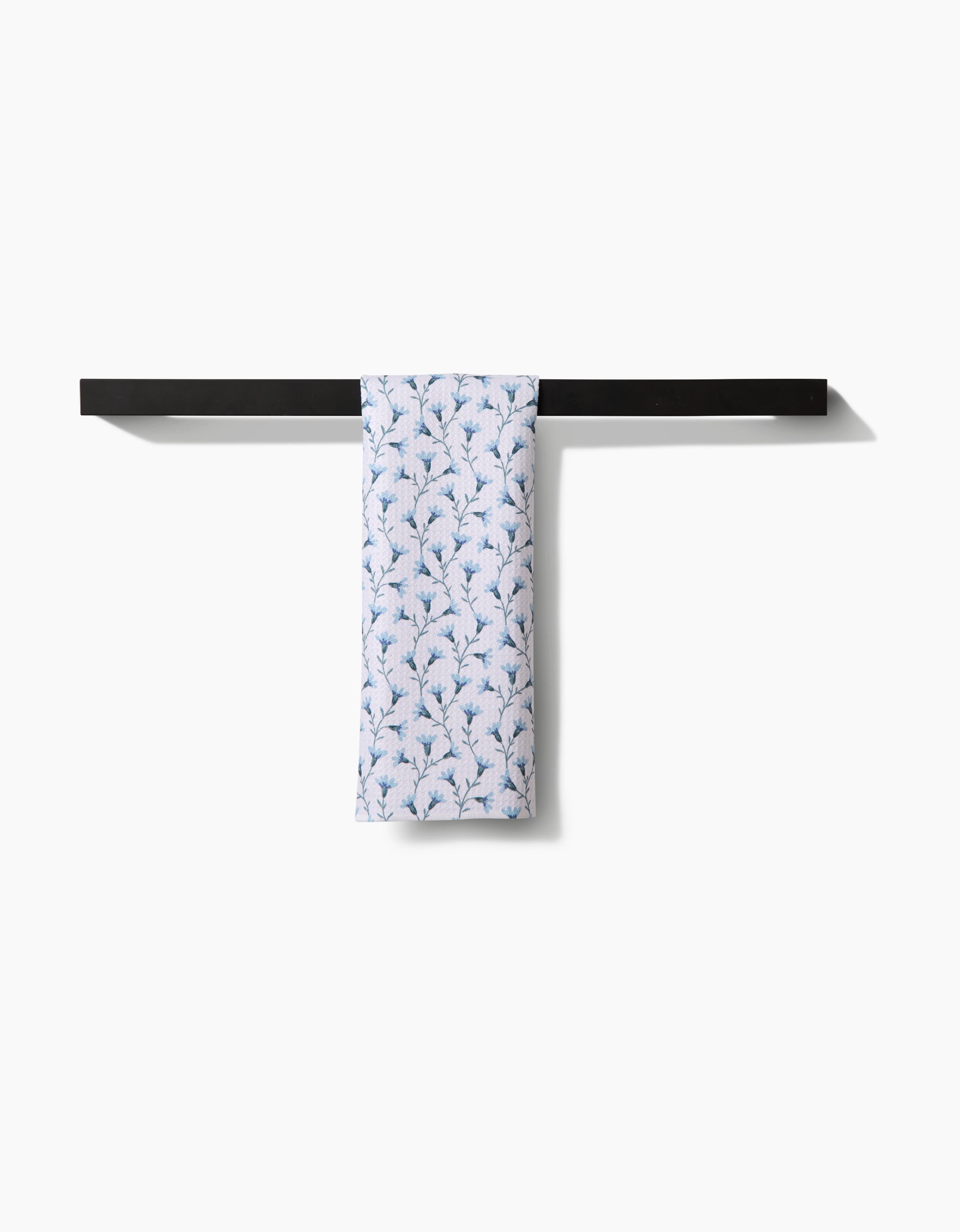 The Trailing Flowers in Blue bar towel by Teri the Butter, featuring a delicate white and blue leafy pattern on light blue recycled fabric, hangs over a sleek black towel bar against a plain white background.