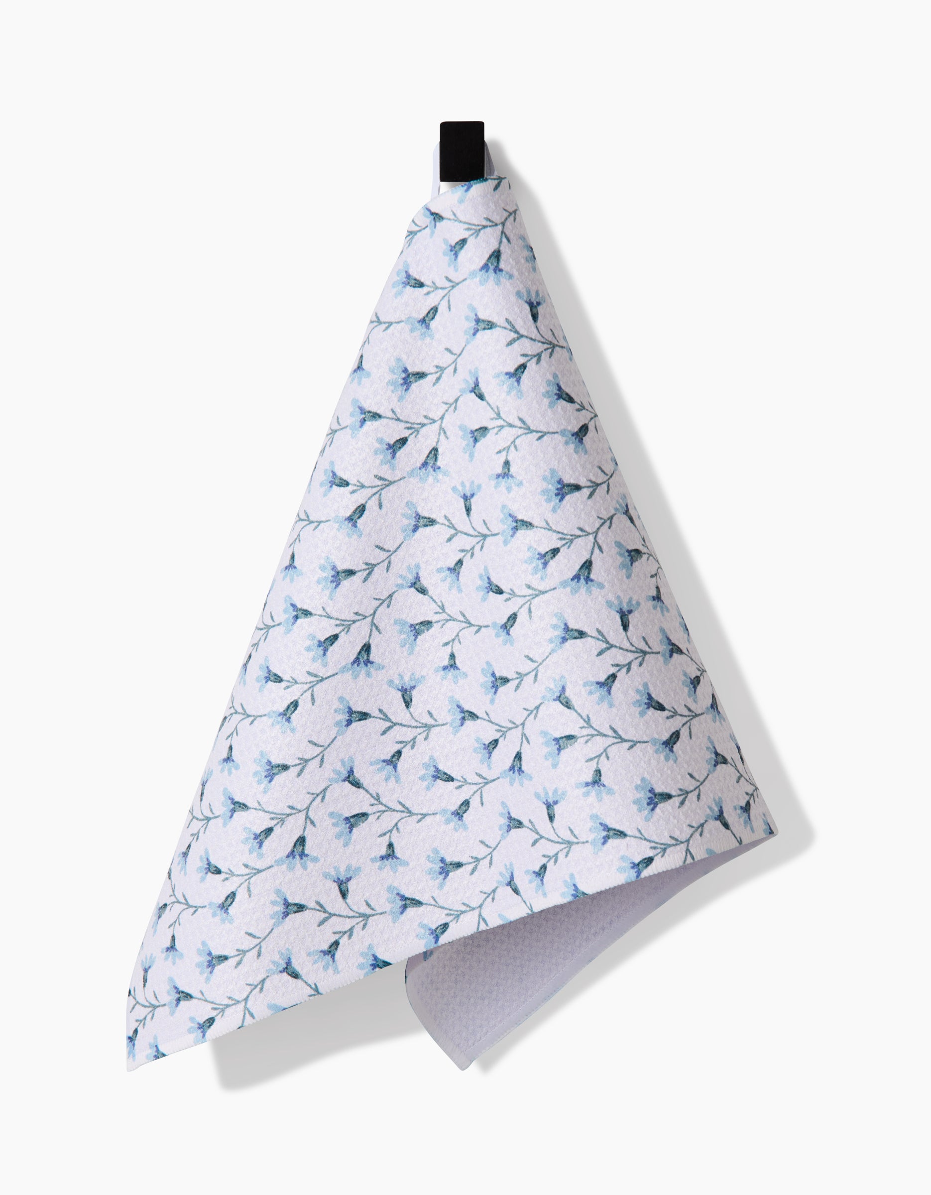 The Trailing Flowers in Blue kitchen towel by Teri the Butter, made from Geoweave fabric, features a blue floral pattern on white and hangs from a black loop against a white background.