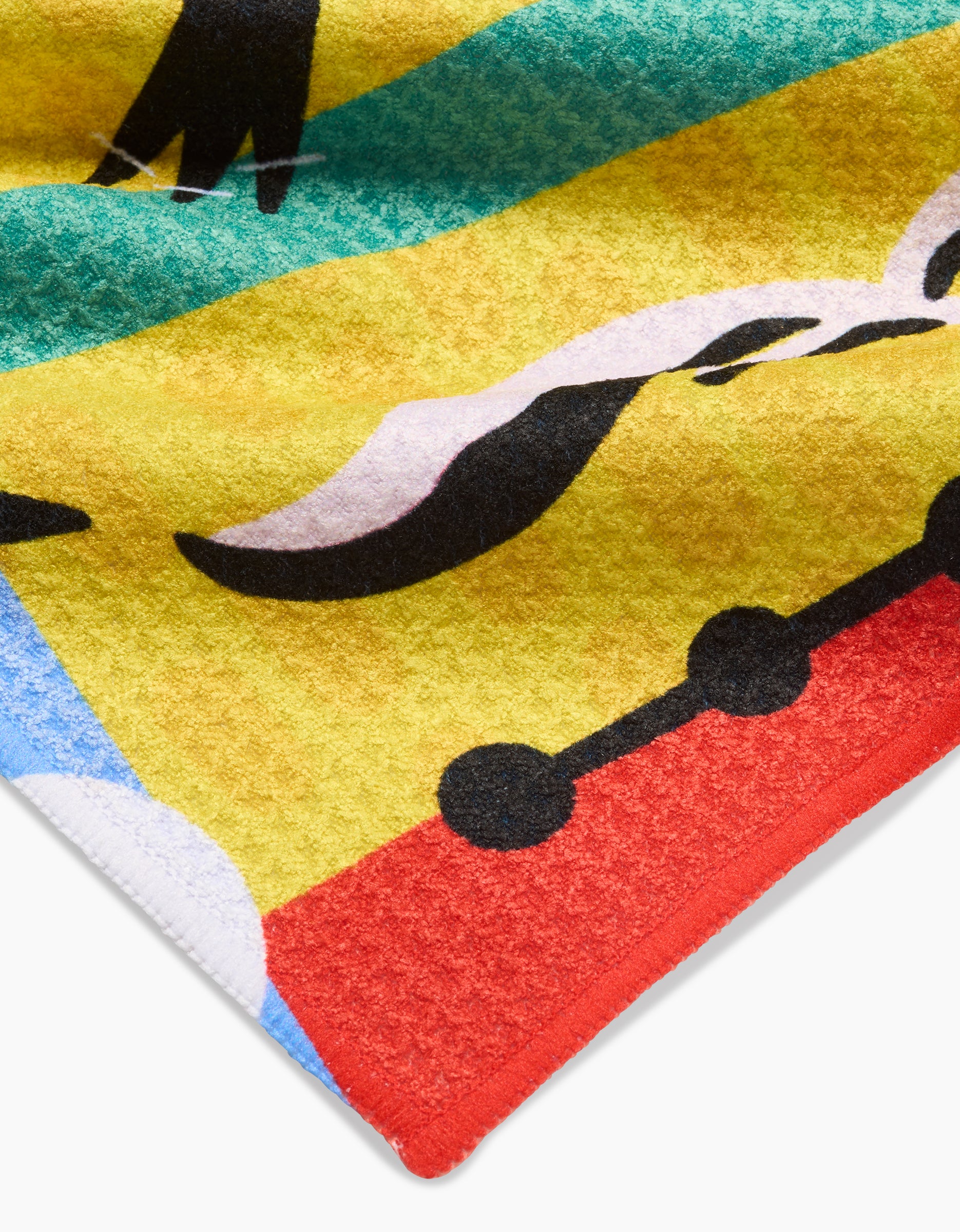 A close-up of the Tuiuiú Bar Towel by Camila Leão showcases abstract black shapes over yellow, red, blue, and green. Curved and dotted lines highlight its ultra-absorbent Geoweave fabric with a textured finish.