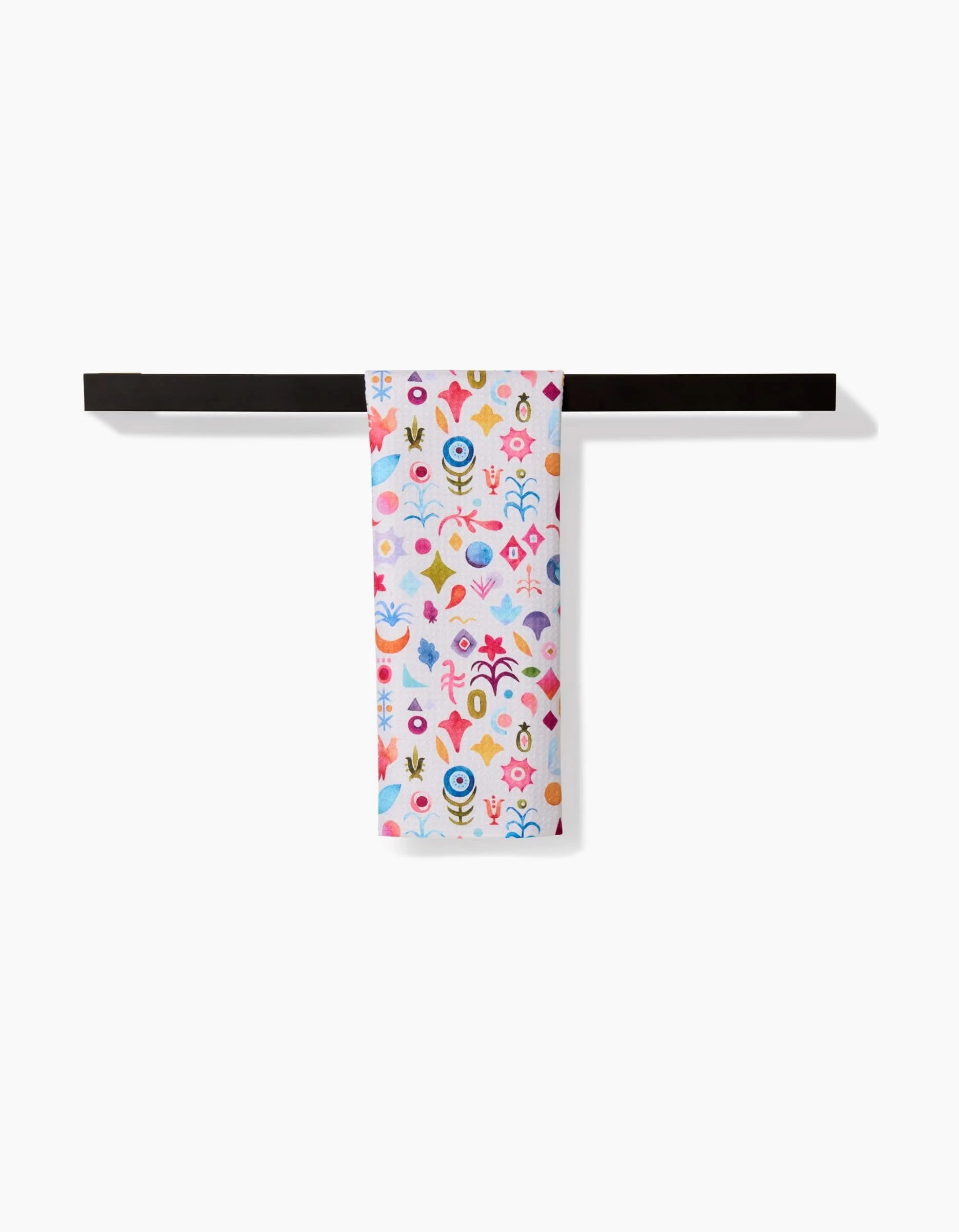 The Tula bar towel by Maayan Alper-Swan, made from recycled materials and decorated with abstract floral patterns, hangs neatly on a dark towel bar against a white background.