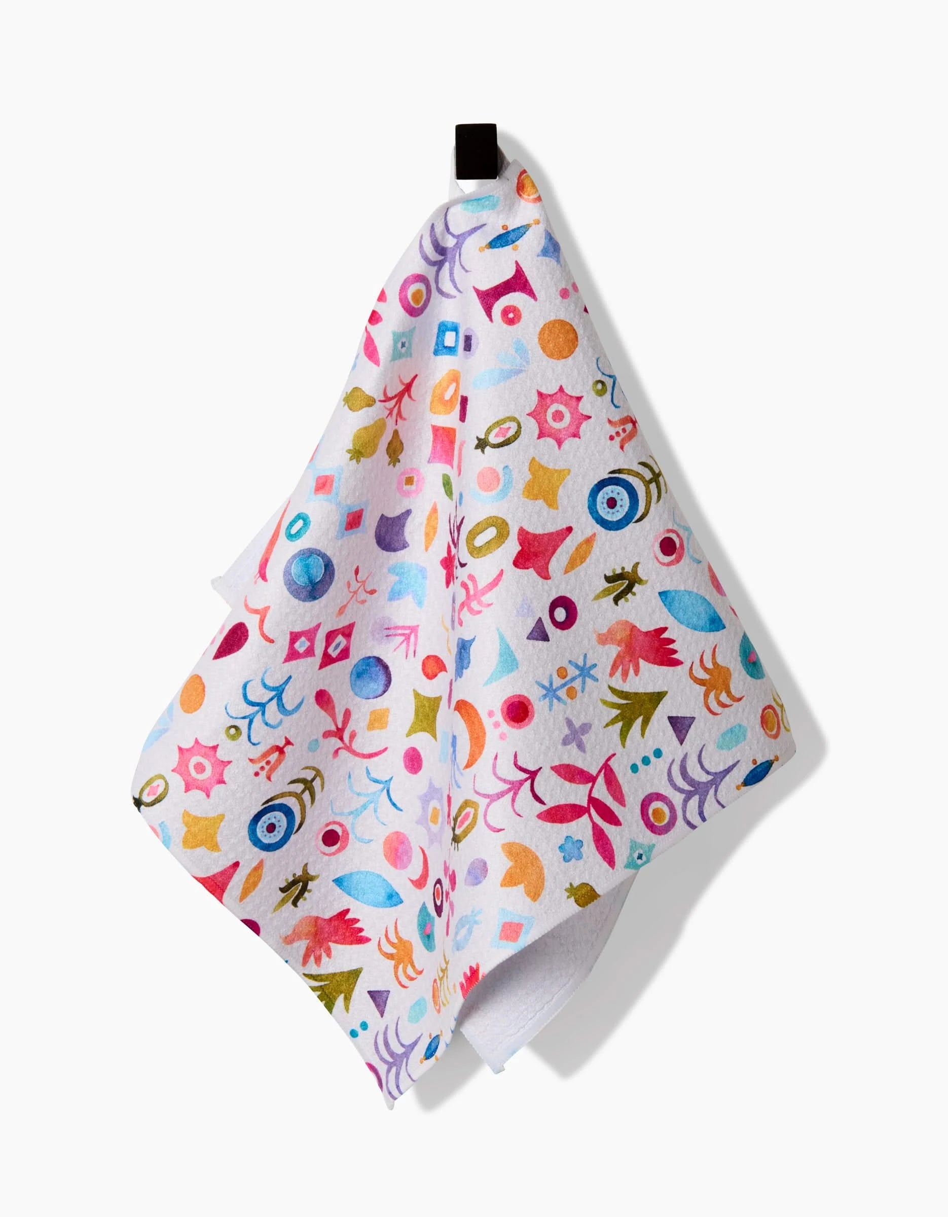 The Tula bar towel by Maayan Alper-Swan is white, made from recycled materials, and showcases colorful abstract shapes—eyes, leaves, and geometric patterns—with a black hanging loop against a plain background.