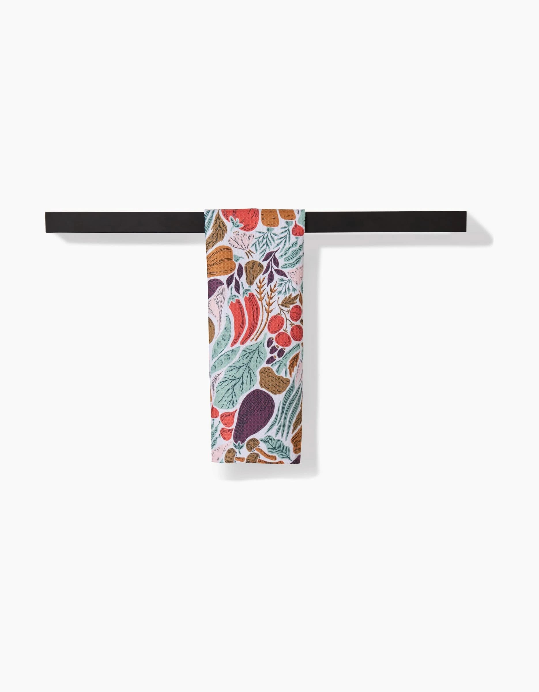 The Twila bar towel by Amy MacCready, featuring a vibrant vegetable print on Geoweave fabric, is draped over a simple black bar against a plain white background.