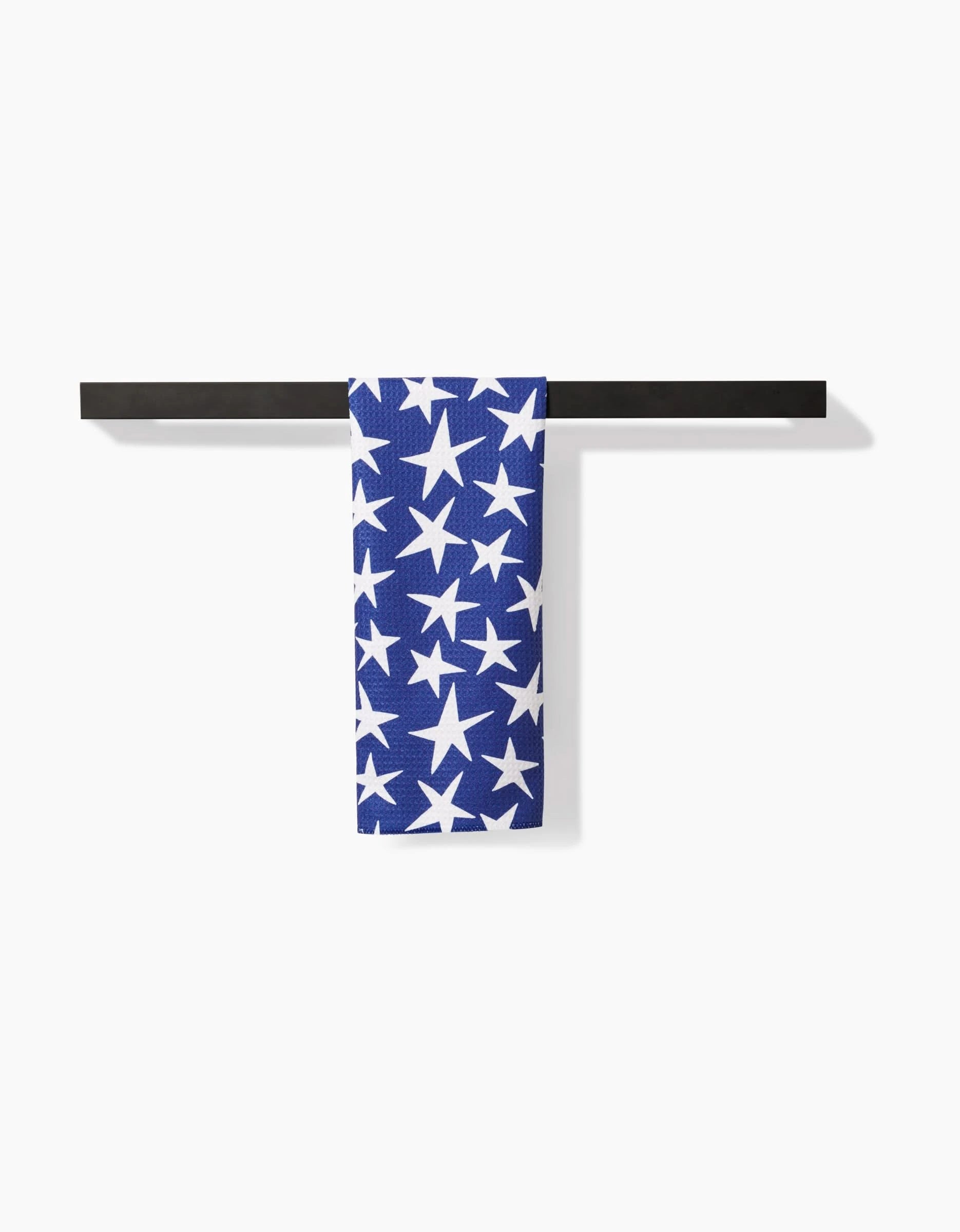 The Mindfulnice USA Stars bar towel features a blue background with white stars, made from soft Geoweave fabric for superior absorbency. It is neatly draped over a black bar against a plain white backdrop.