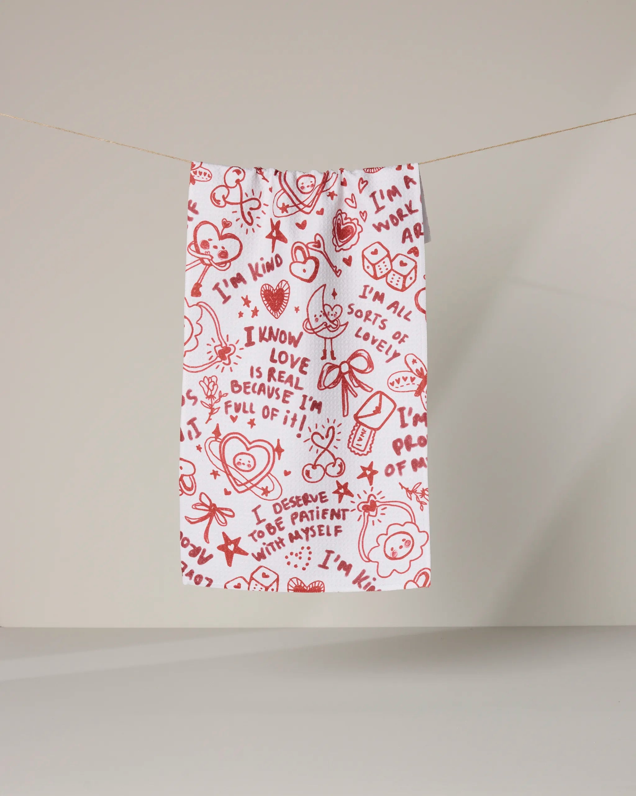 The Geometry Valentines Affirmations towel is ultra-absorbent, white with red doodles and uplifting phrases, perfect for adding cheer to any space.