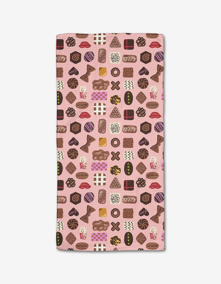 The Elisabeth Wing “Valentine’s Chocolates” Bar Towel features a pink background with a colorful pattern of assorted chocolates and candies. Made from Geoweave fabric, the rectangular towel is shown flat on a white surface.