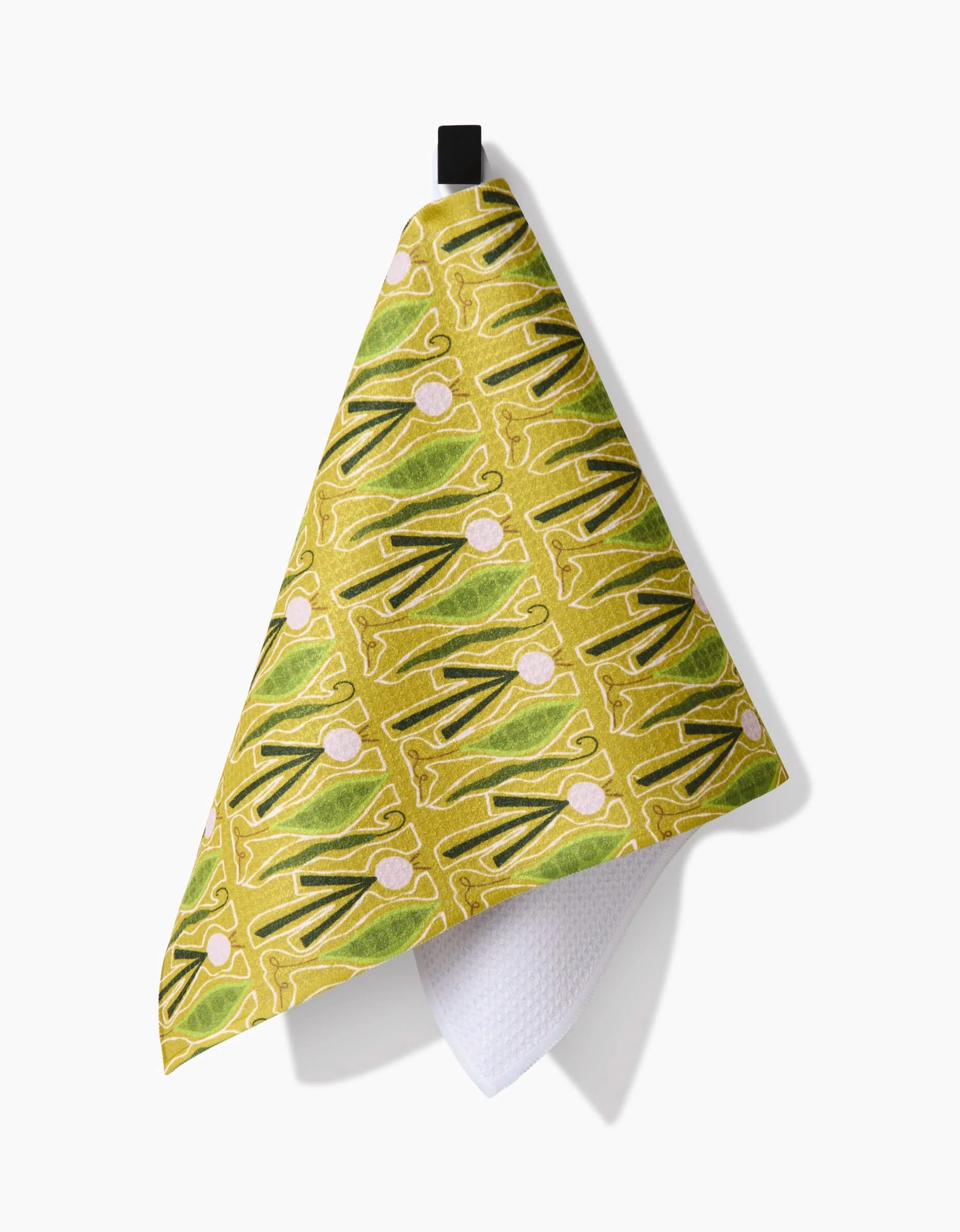 A yellow Veg on Parade kitchen towel by Lizzie Clark, made from Geoweave fabric, features a green and pink abstract pattern. It hangs from a black loop with its white textured underside visible against a white background.