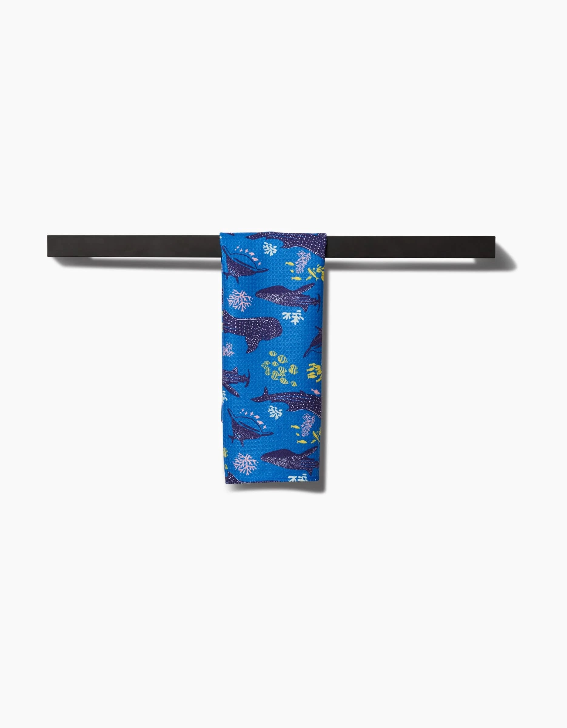 The Elisabeth Wing Whale Shark bar towel features a pattern of whales and fish in blue and green hues, crafted from quick-drying Geoweave fabric, and is shown hanging on a black bar against a white background.