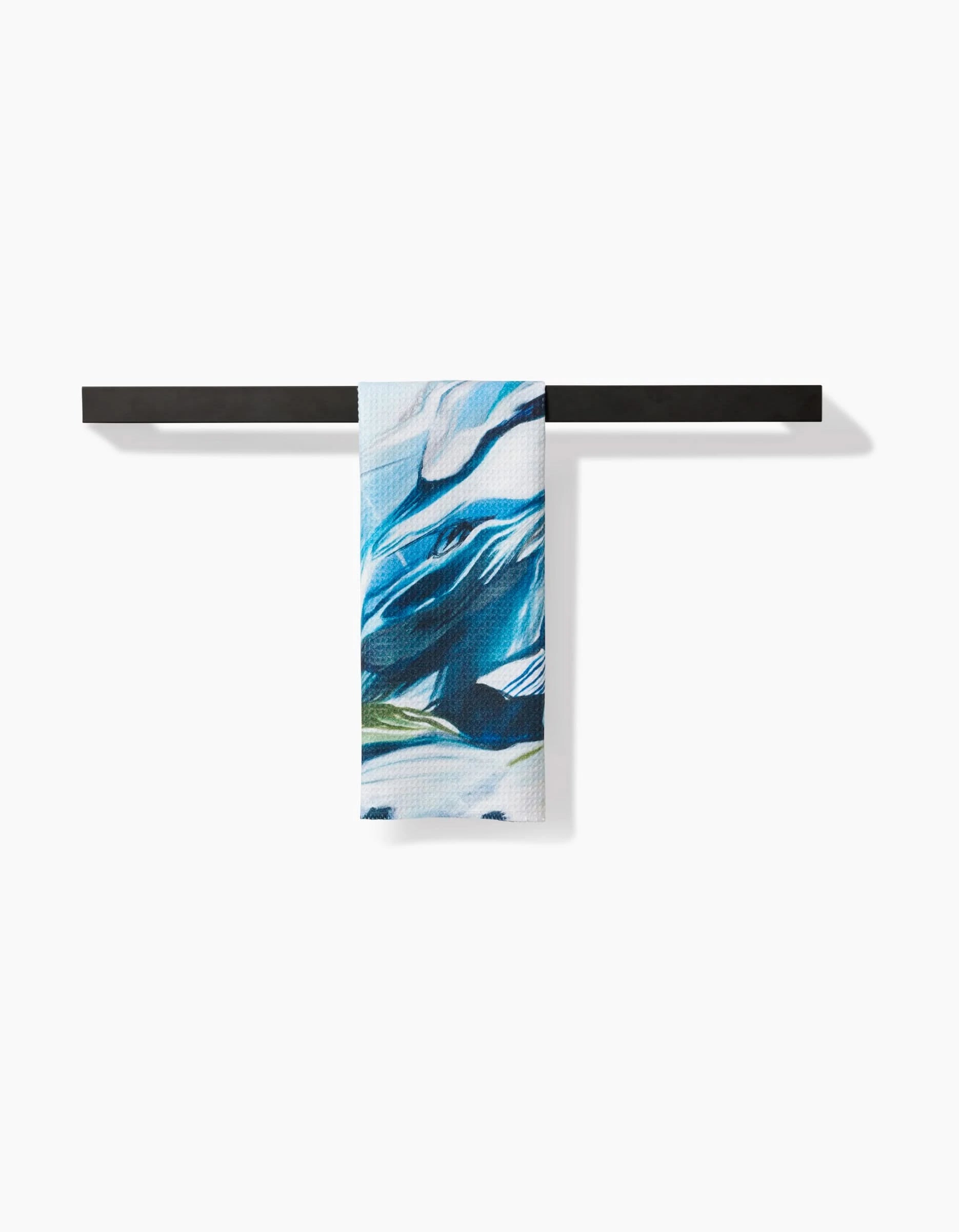 The Where He Laid To Go bar towel by Kelly Peters, featuring blue, white, and green abstract patterns on recycled material, hangs neatly over a black horizontal bar against a plain white background.