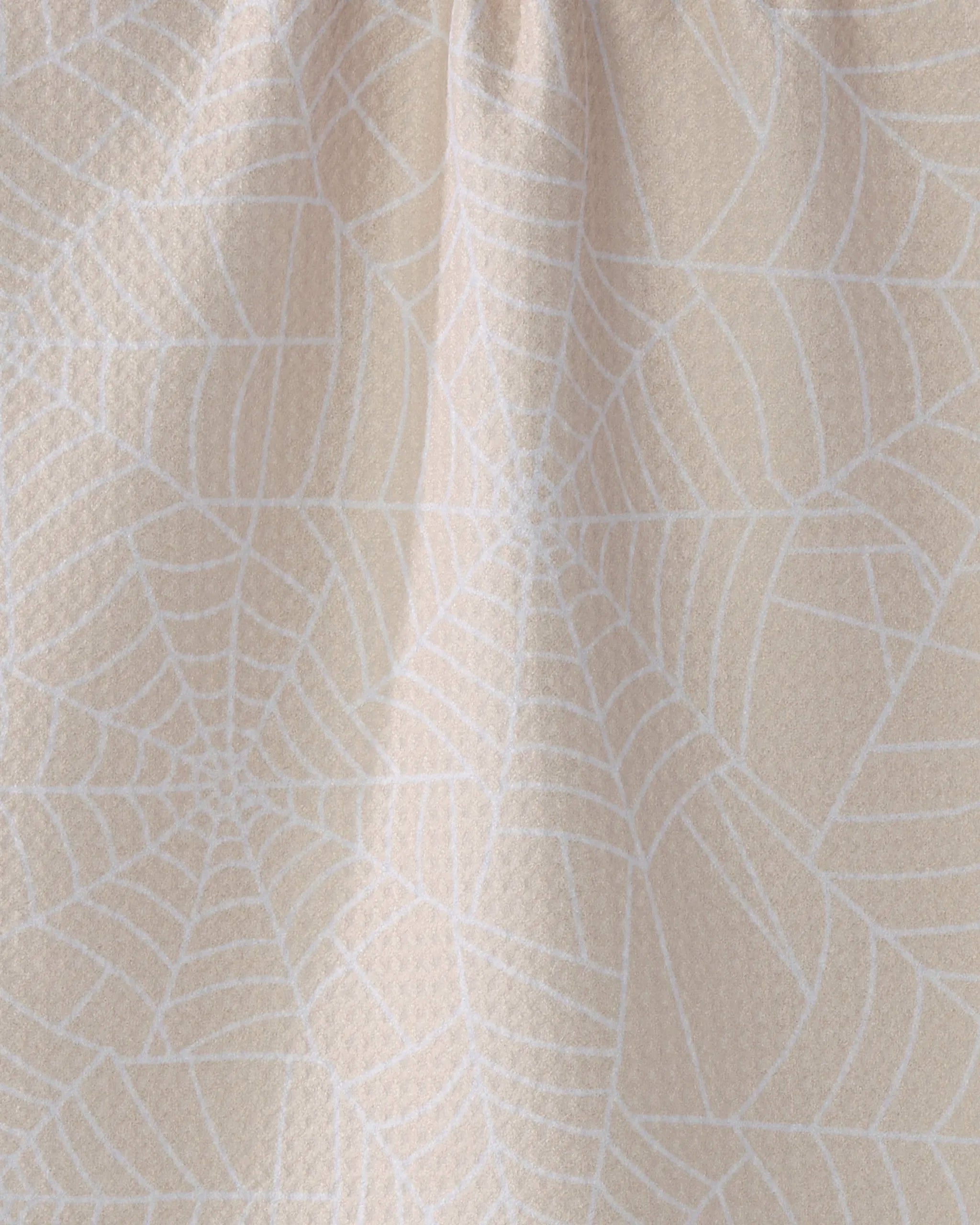 A close-up of Whisper Web by Geometry shows pale beige recycled fabric with a subtle white geometric spiderweb pattern and gentle wrinkles near the top center.