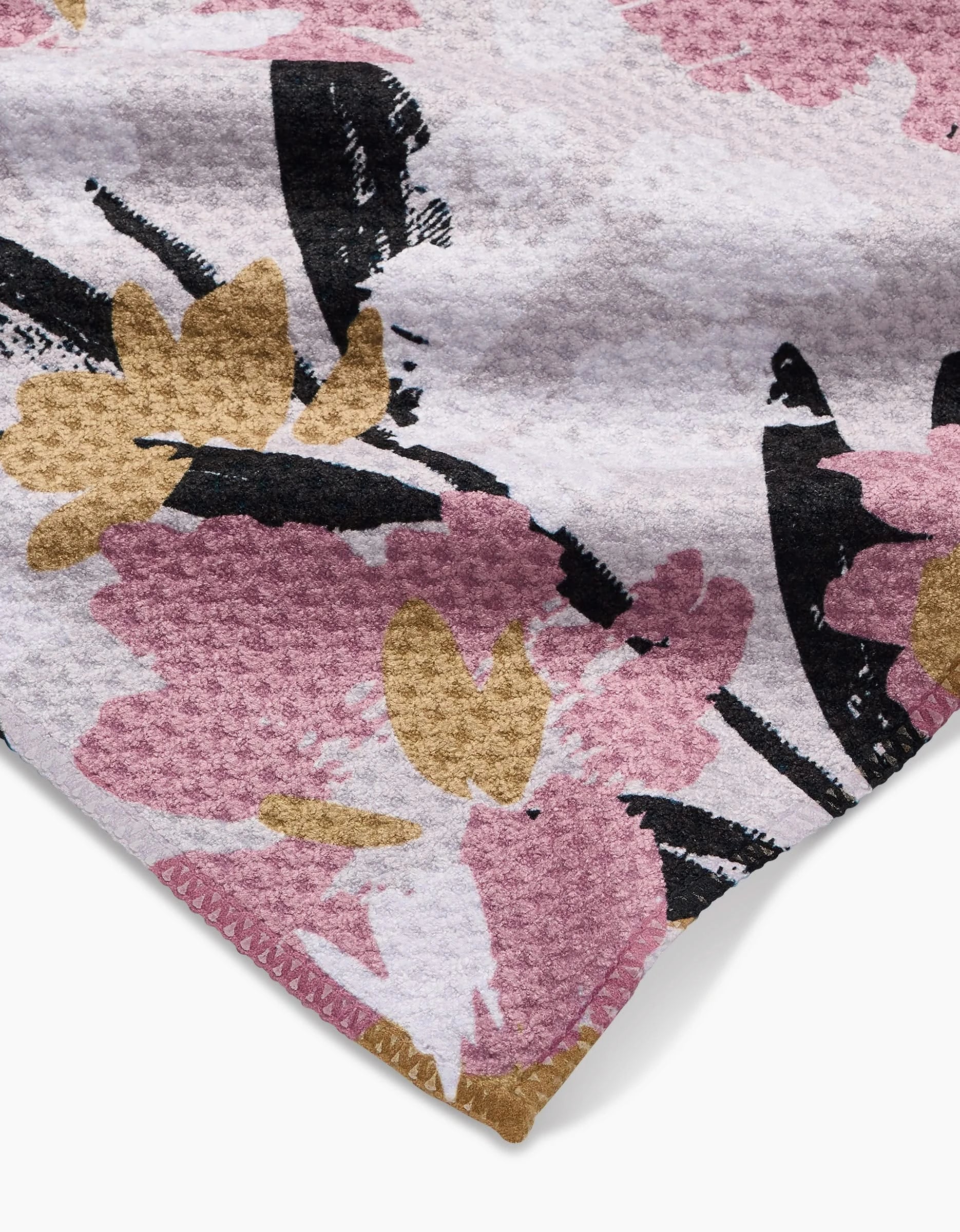 A close-up of Toboggan Avenue’s Wilderness Floral bar towel, featuring textured Geoweave fabric with pink, gold, black, and white floral patterns. The corner and detailed edge stitching are clearly visible.
