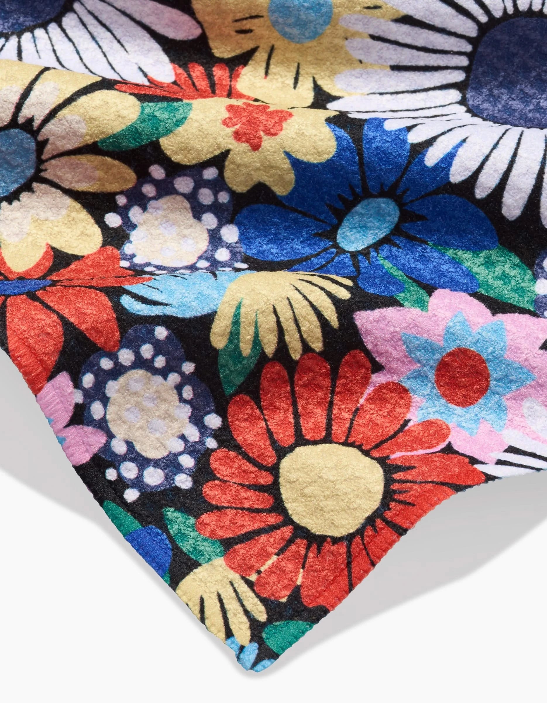 A close-up of Claire Iglesiass Wildflowers Bouquet Bar Towel, made from Geoweave fabric and featuring a bold, colorful floral pattern with vibrant red, blue, yellow, white, and green flowers on a black background.